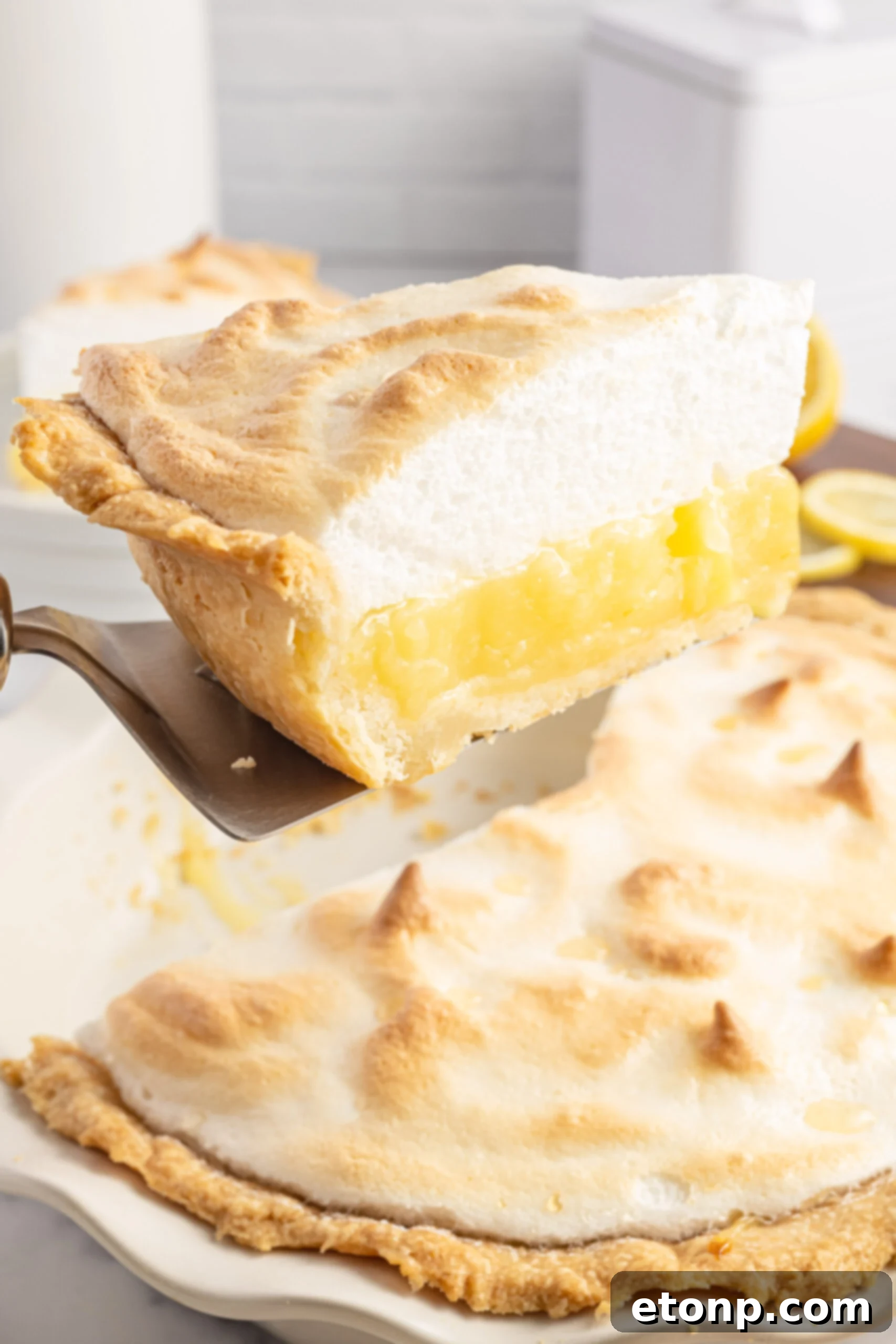A slice of perfect lemon meringue pie being lifted from the dish with a silver spatula, showing its structural integrity.