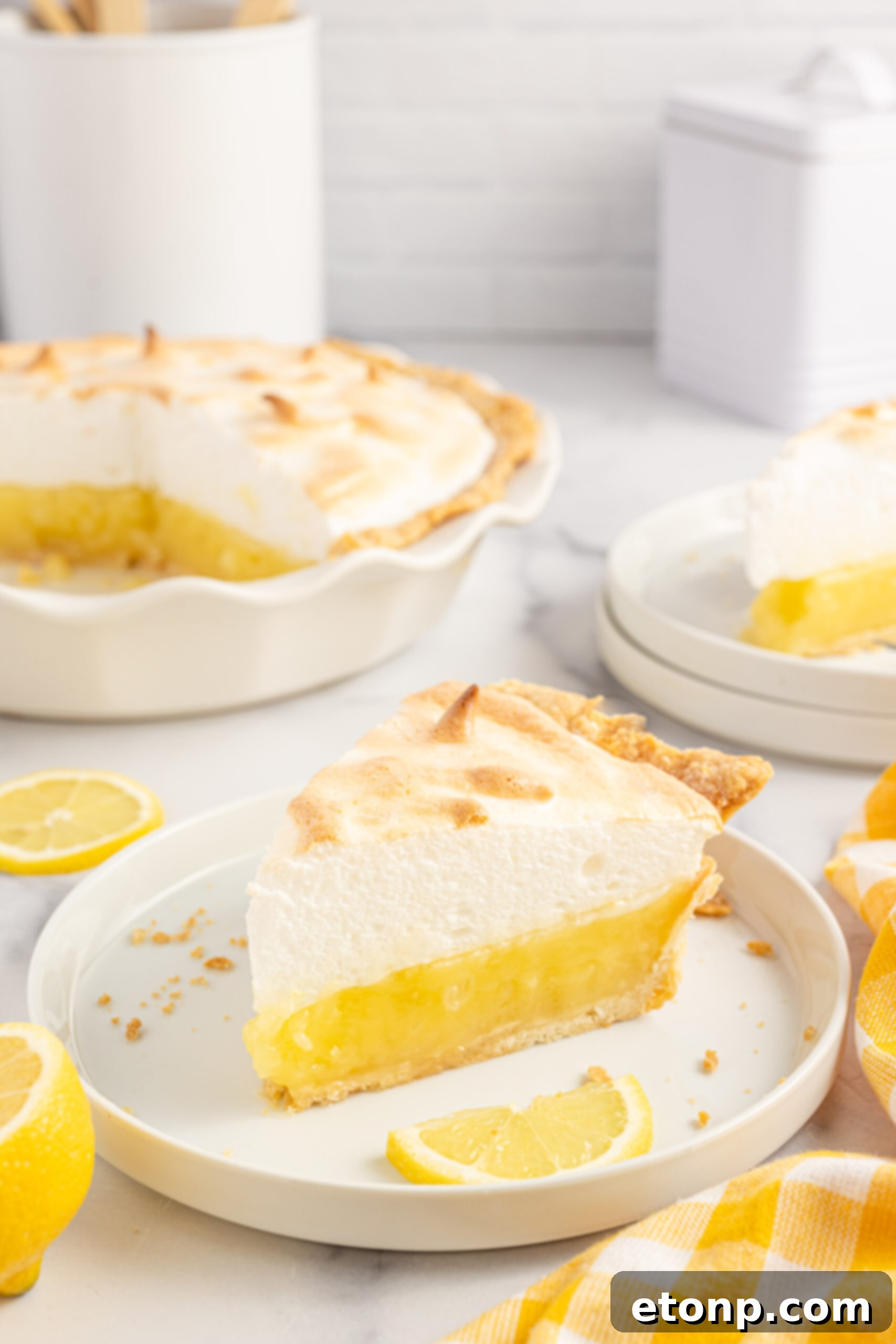 A beautiful slice of lemon meringue pie on a white plate, accompanied by fresh lemon wedges.