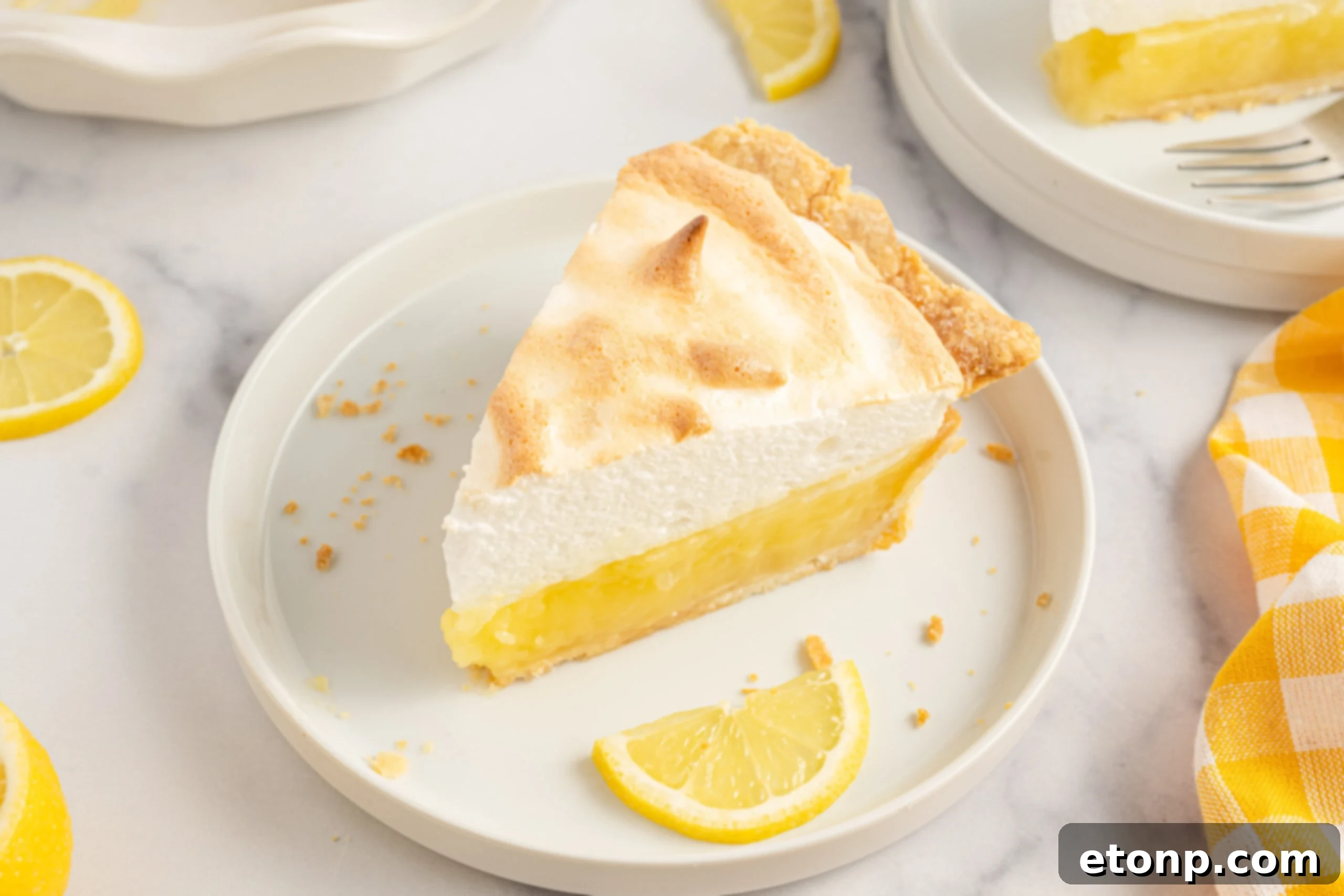 A tempting slice of lemon meringue pie on a white plate with fresh lemon slices, highlighting the golden meringue.