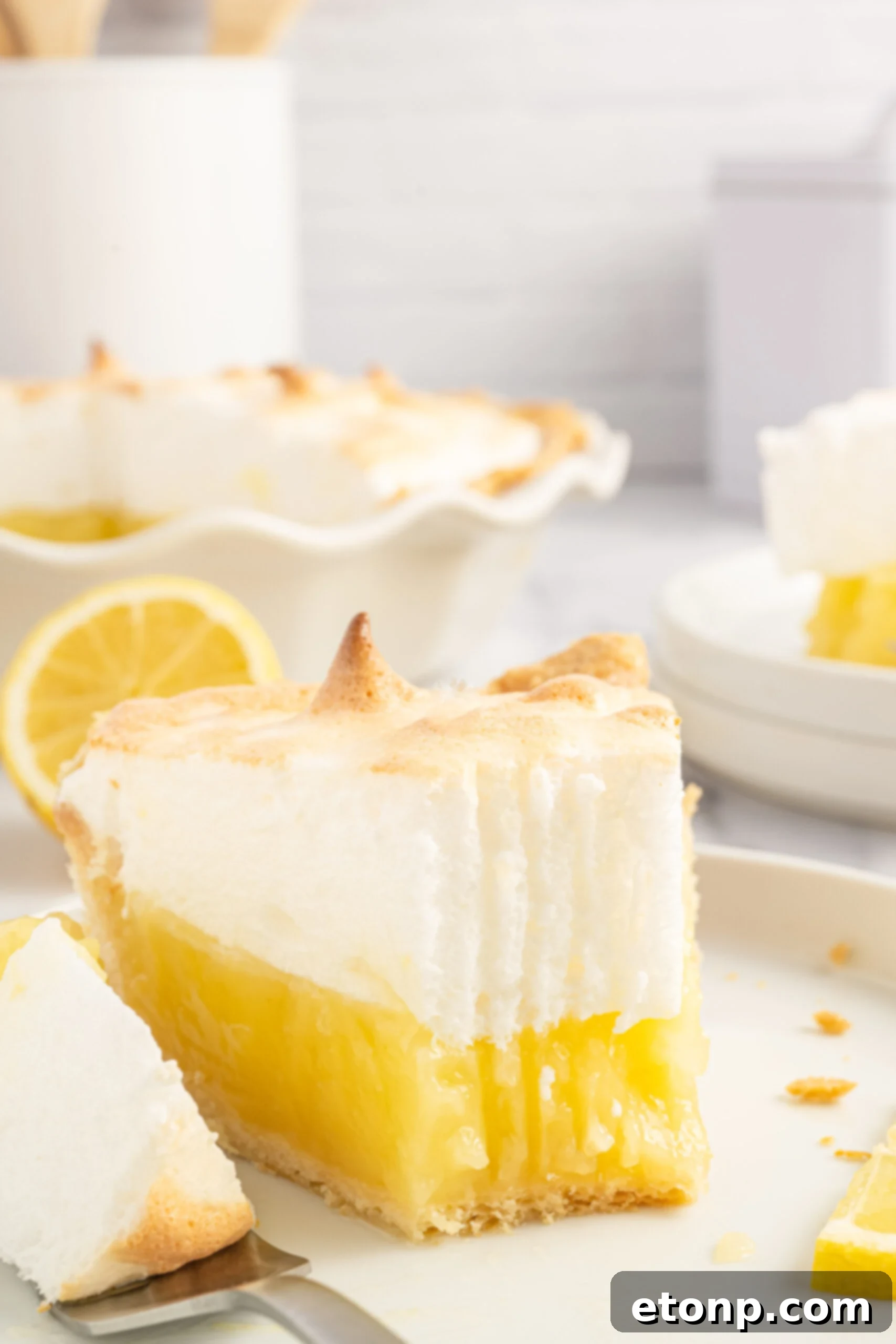 A close-up shot of a bite taken from a slice of fresh lemon meringue pie, showing the vibrant layers.