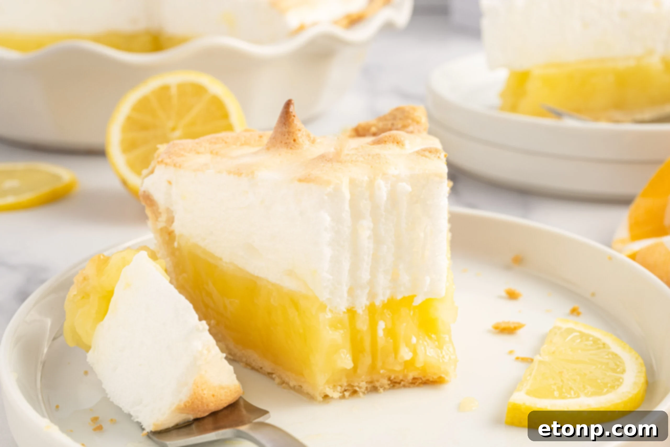 A delectable slice of lemon meringue pie on a white plate with a bite taken out, showcasing the distinct layers of flaky crust, tangy lemon filling, and light, golden meringue.