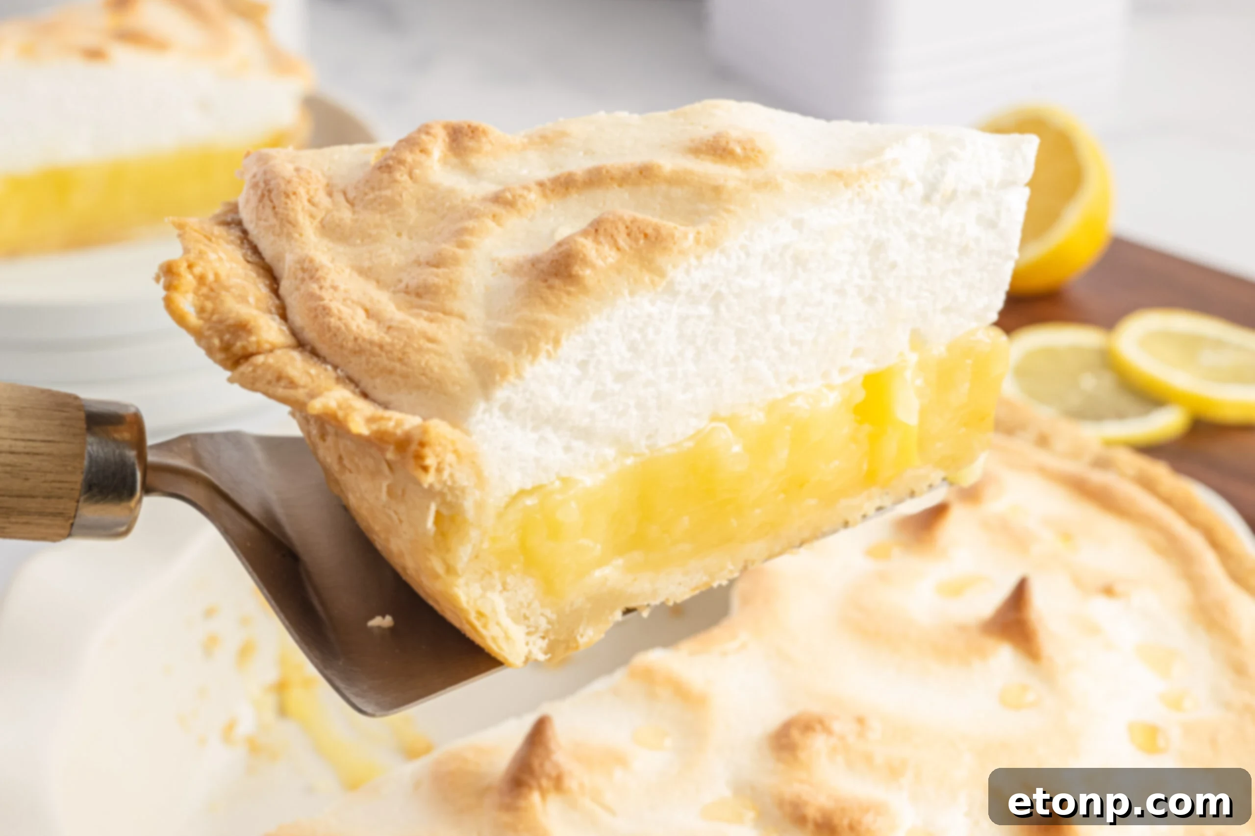 A slice of lemon meringue pie being served with a silver and wooden spatula.