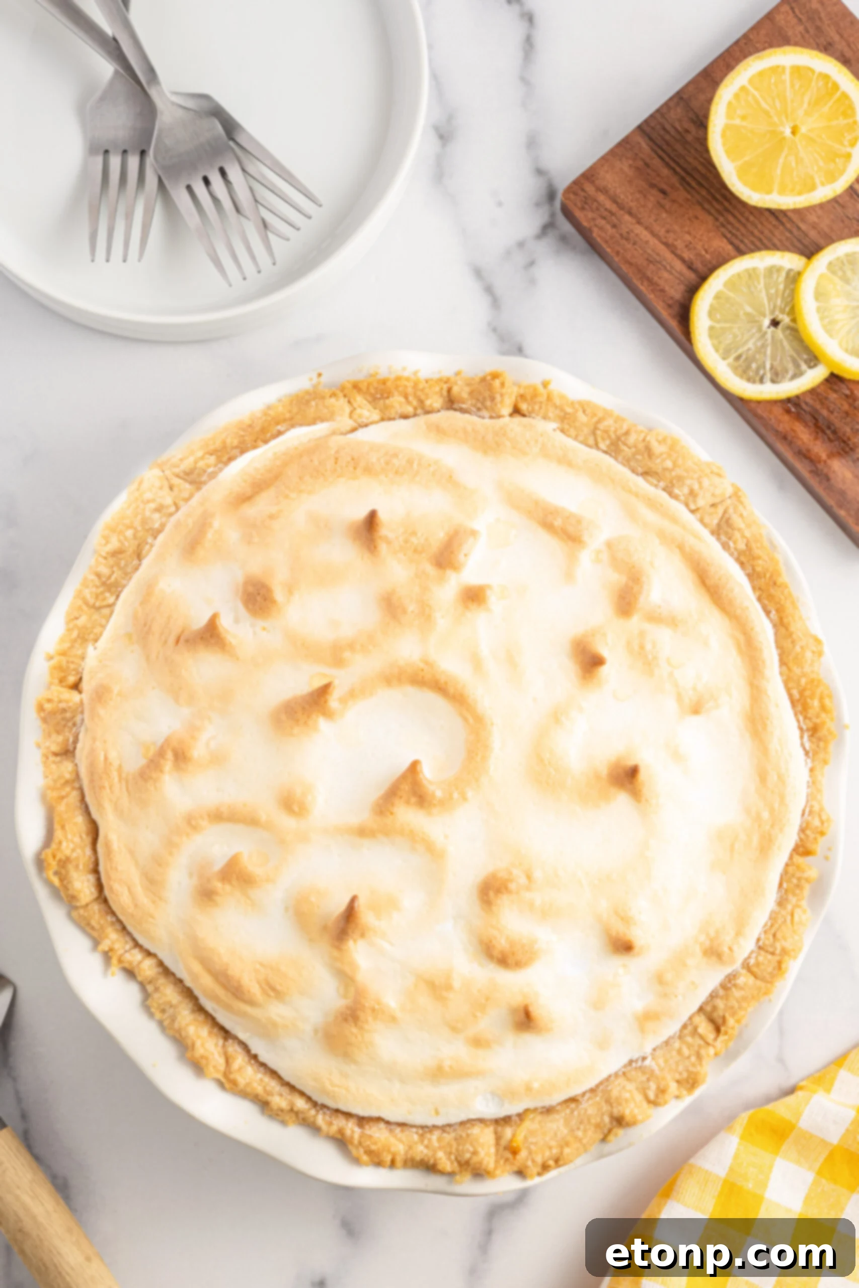 Overhead shot of a beautifully baked lemon meringue pie in a pristine white pie dish, showcasing its perfect golden meringue peaks.