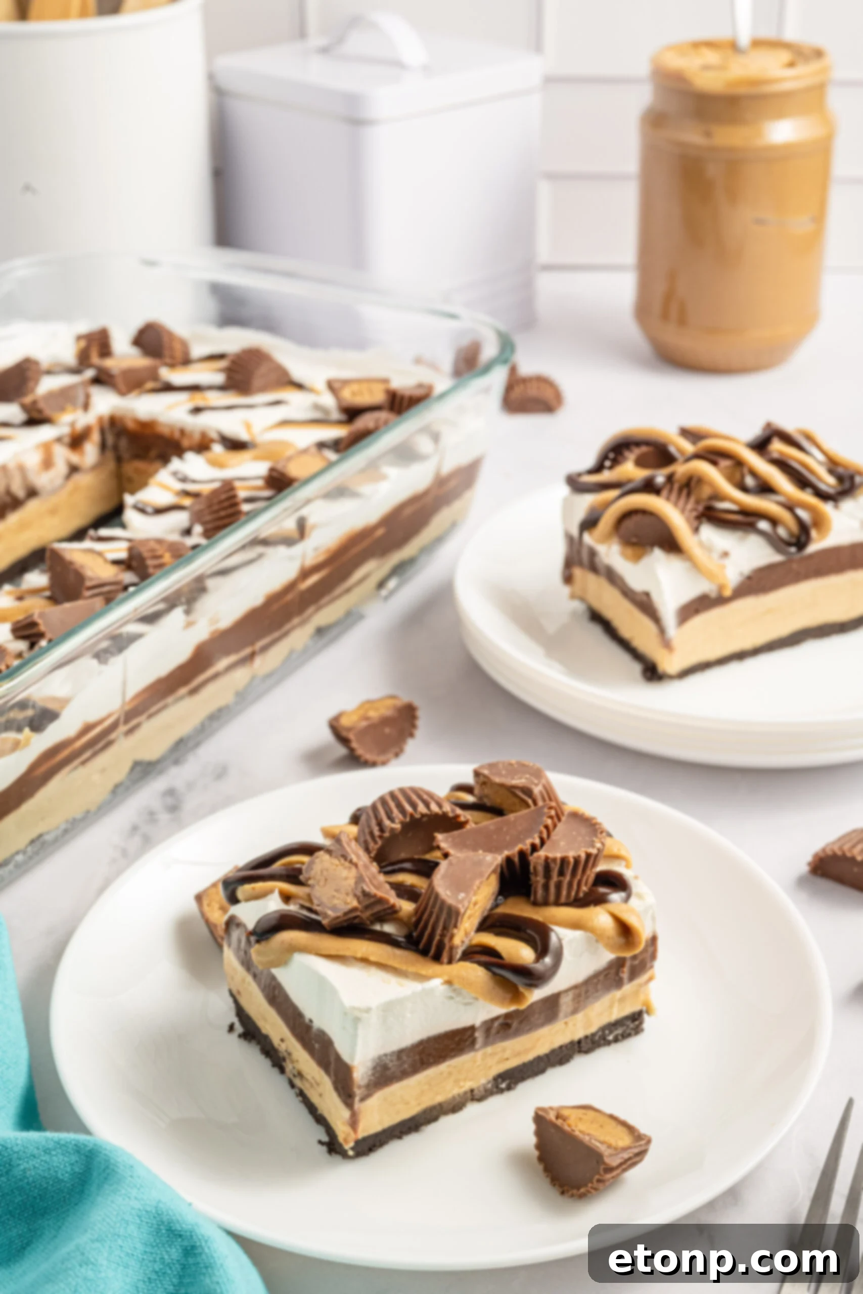 Two pieces of chocolate peanut butter lasagna on two white plates with Reese's cups in the background. 