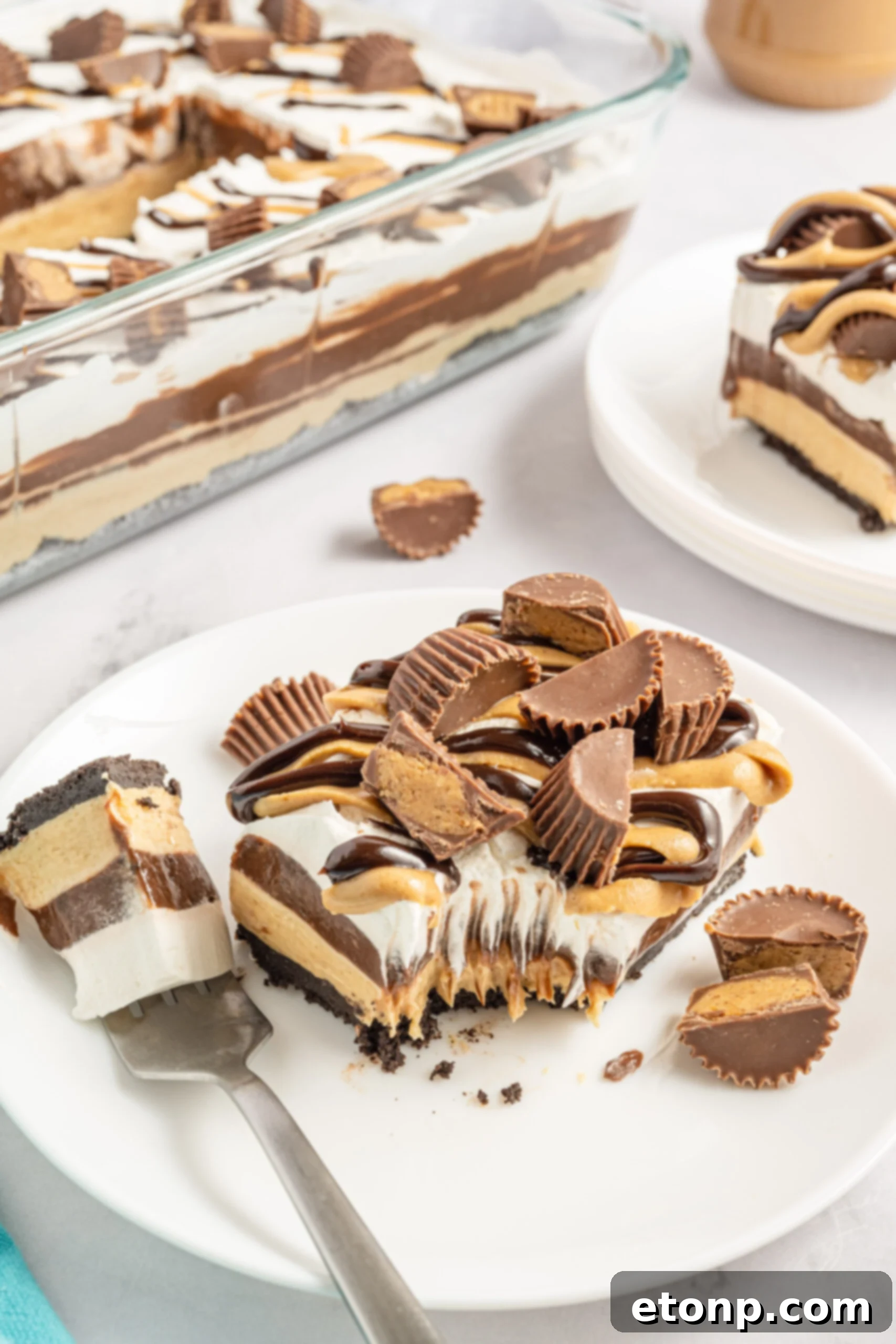 Two pieces of chocolate peanut butter lasagna on two white plates with Reese's cups in the background. 