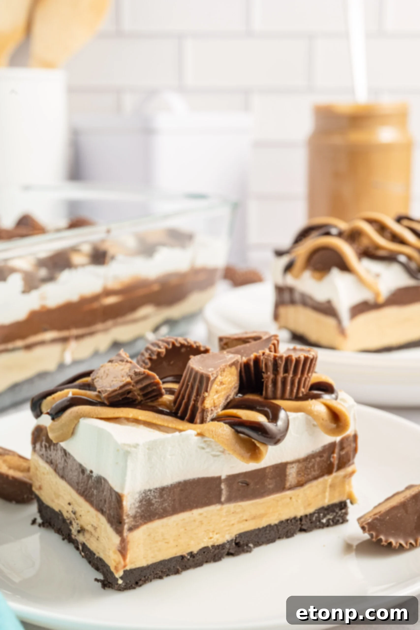 Two pieces of chocolate peanut butter lasagna on two white plates with a jar of peanut butter in the background. 