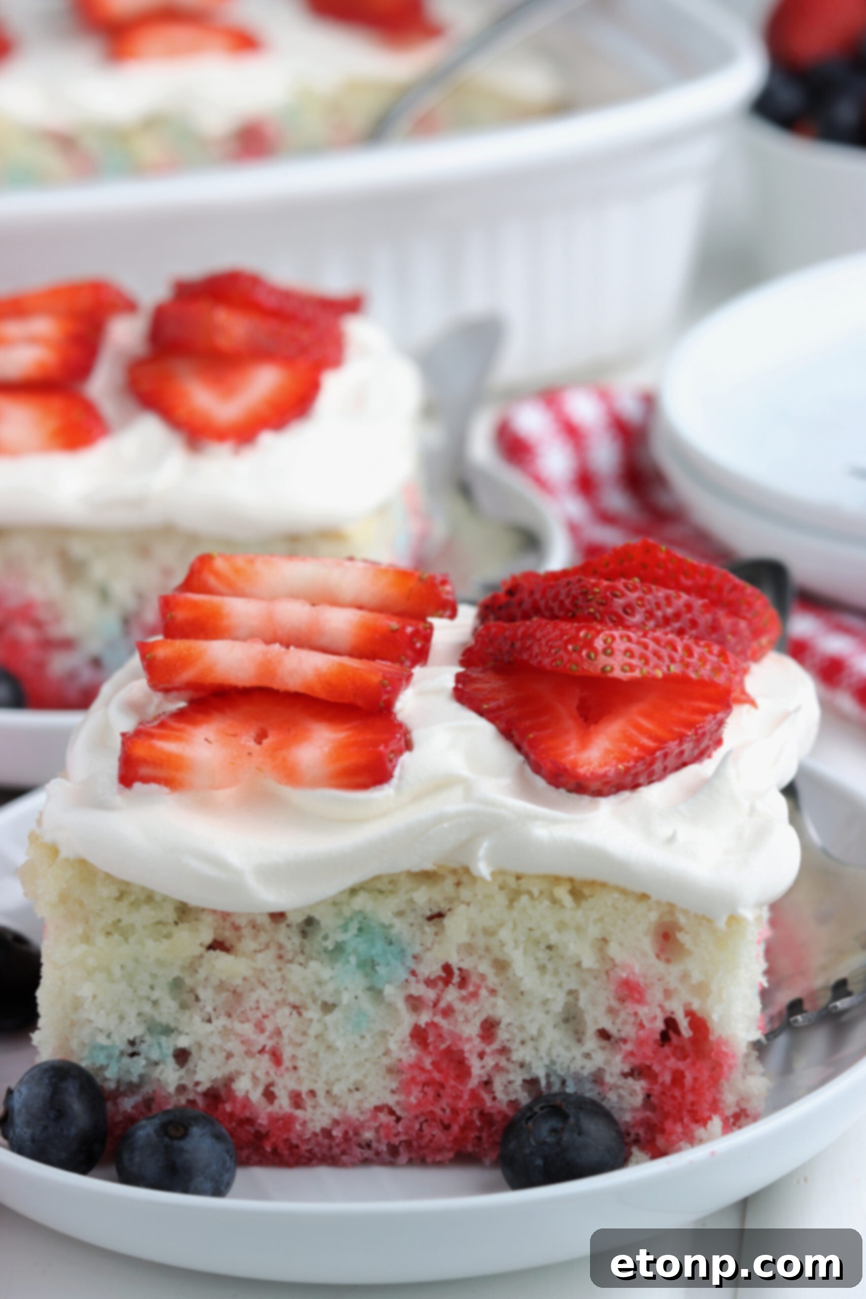 Two pieces of American Flag Cake on two white plates with fresh berries. 