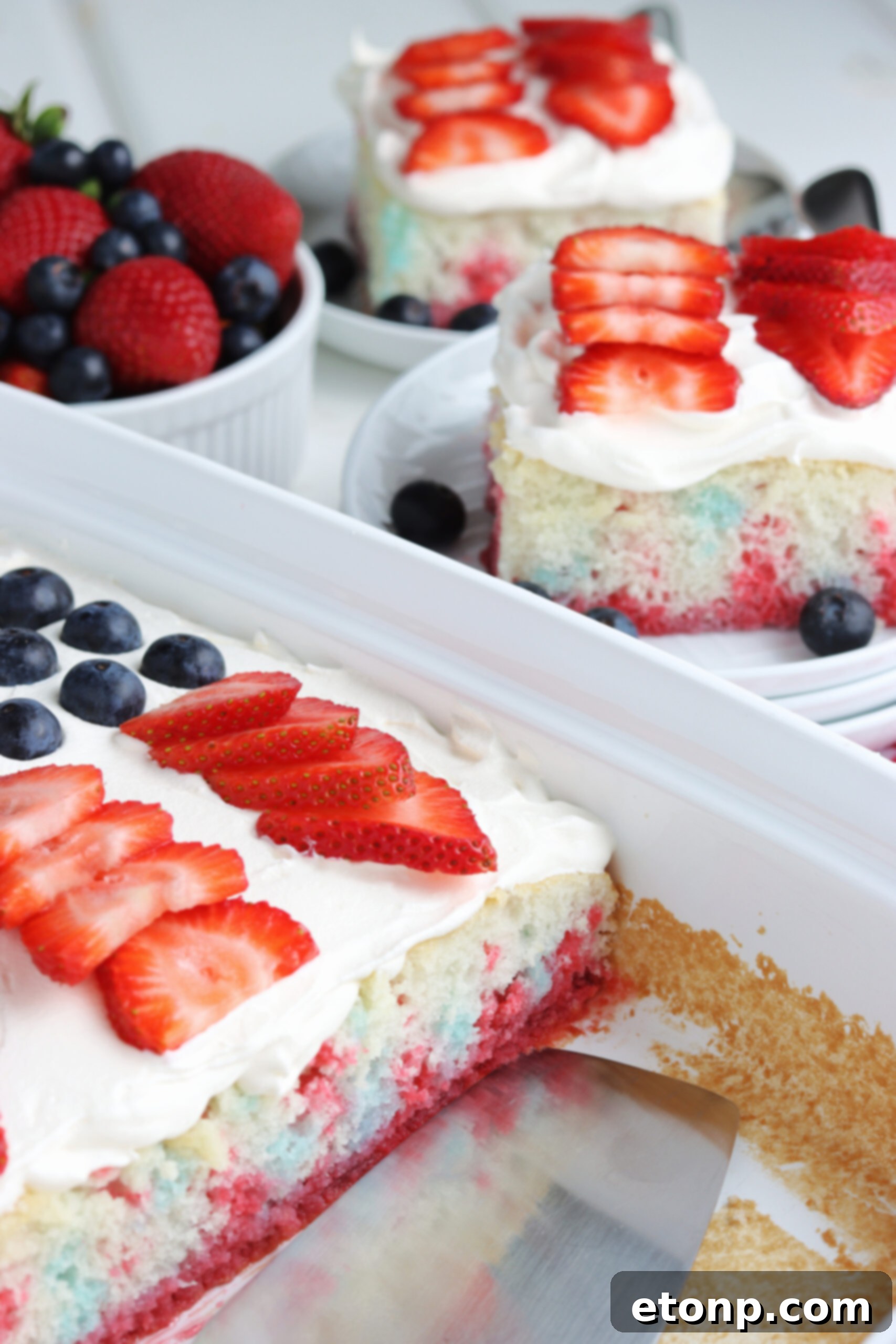 Two pieces of American Flag Cake on two white plates with fresh berries. 