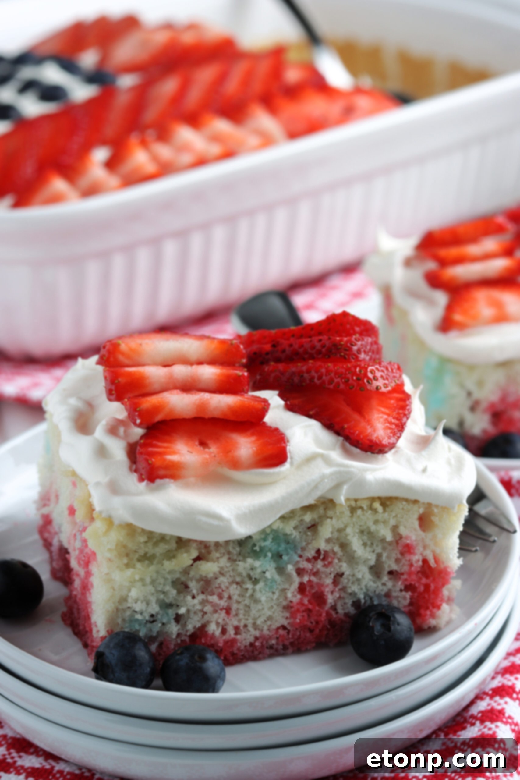 Two pieces of American Flag Cake on two white plates with fresh berries. 