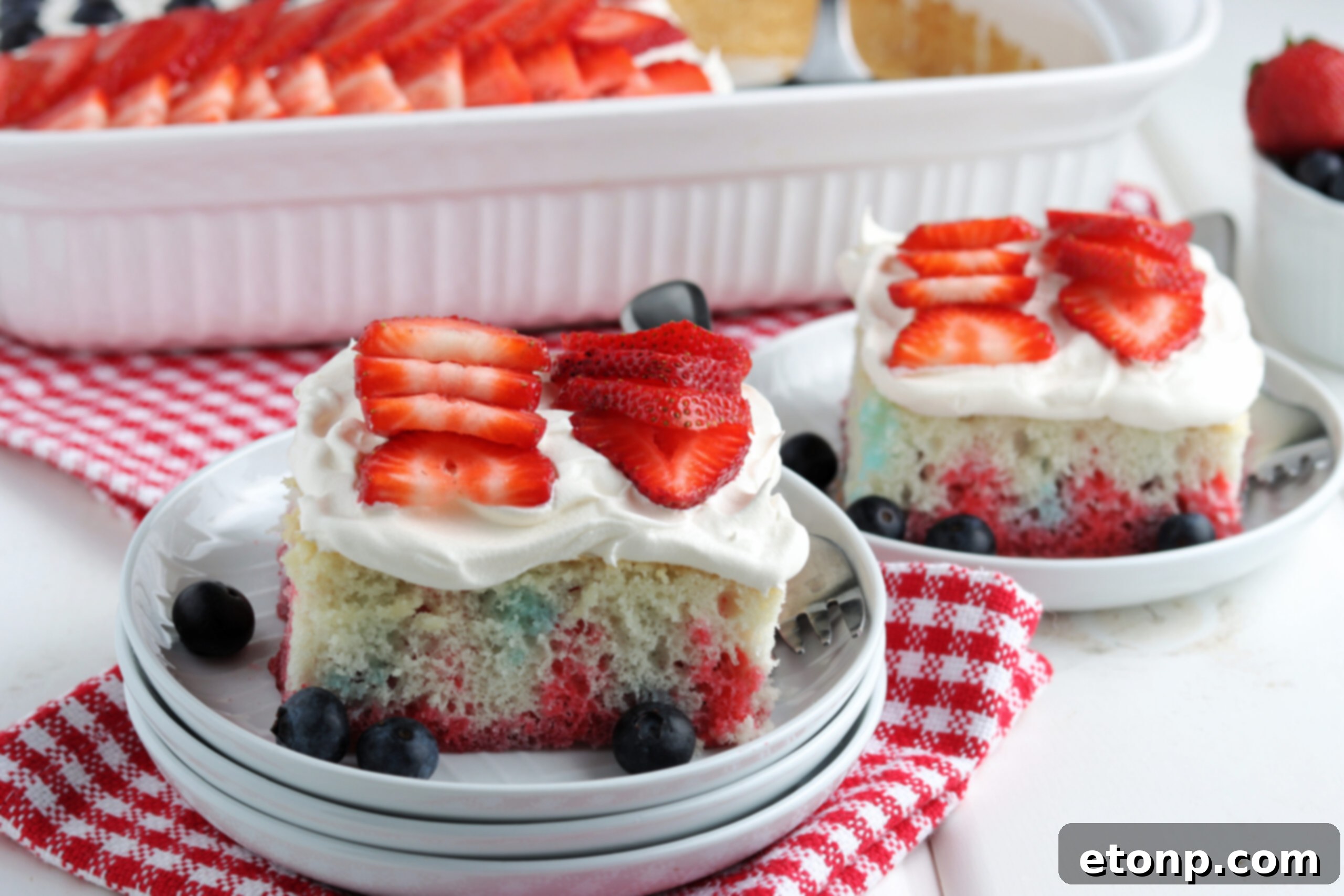 Two pieces of American Flag Cake on two white plates with fresh berries. 