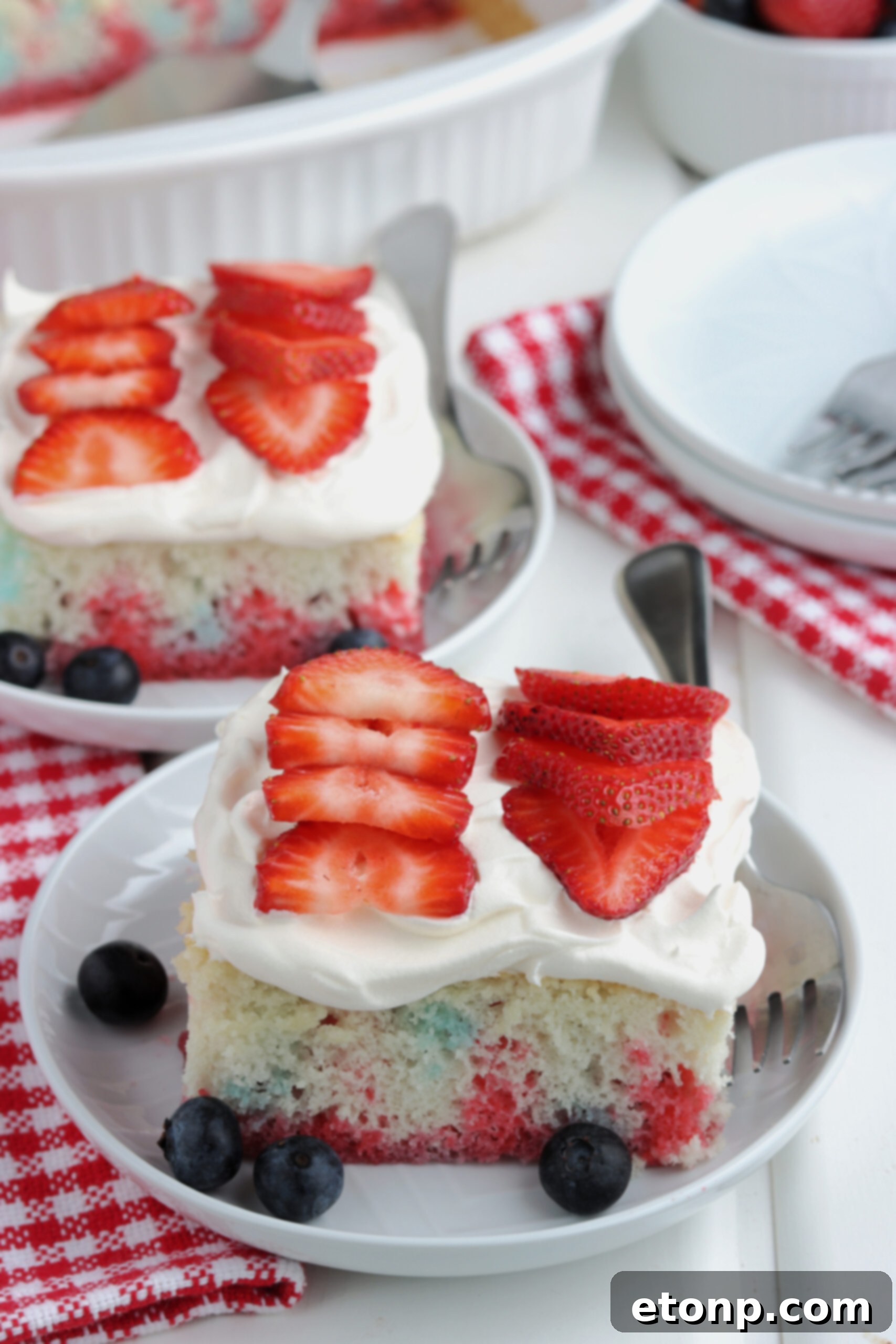 Two pieces of American Flag Cake on two white plates with fresh berries. 