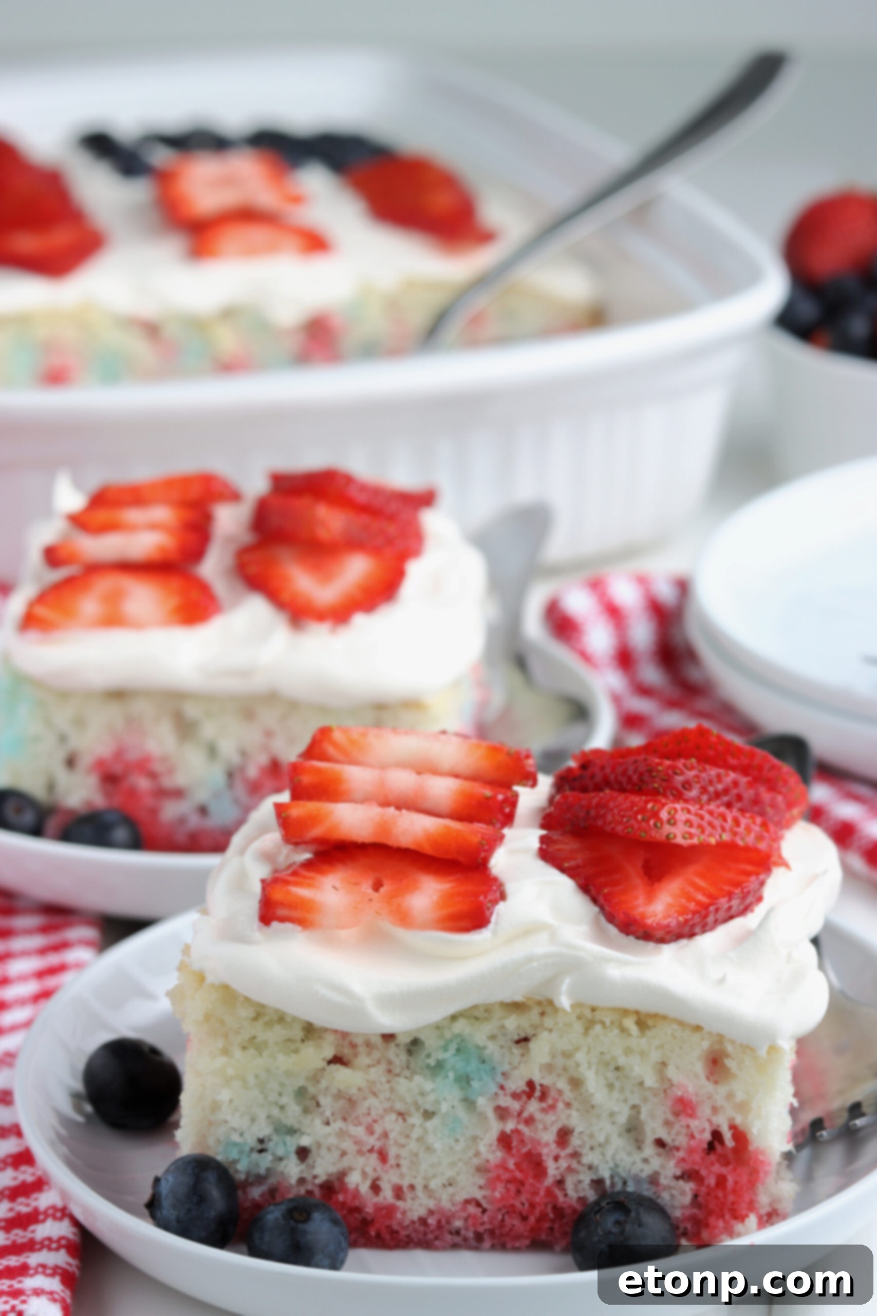 Two pieces of American Flag Cake on two white plates with fresh berries. 