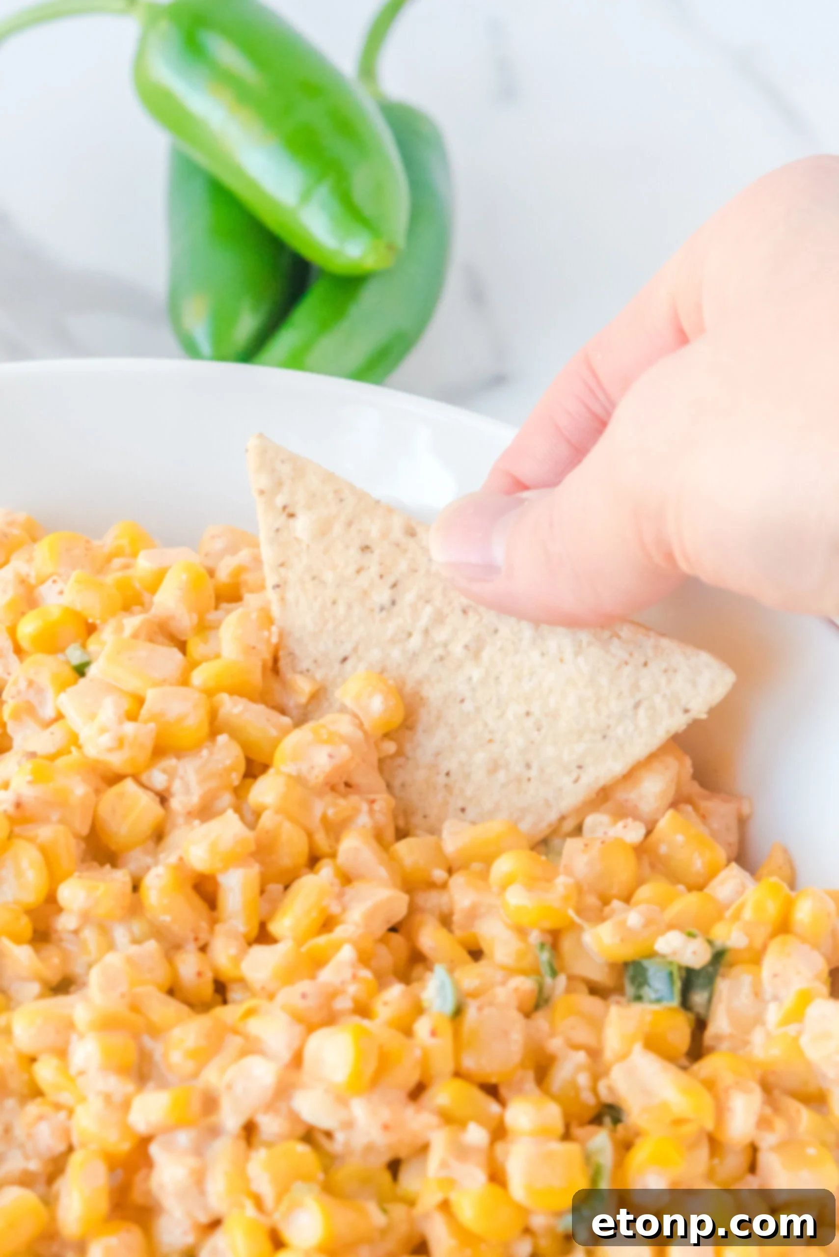 A tortilla chip generously scooping up creamy Mexican Street Corn Salad from a white bowl.