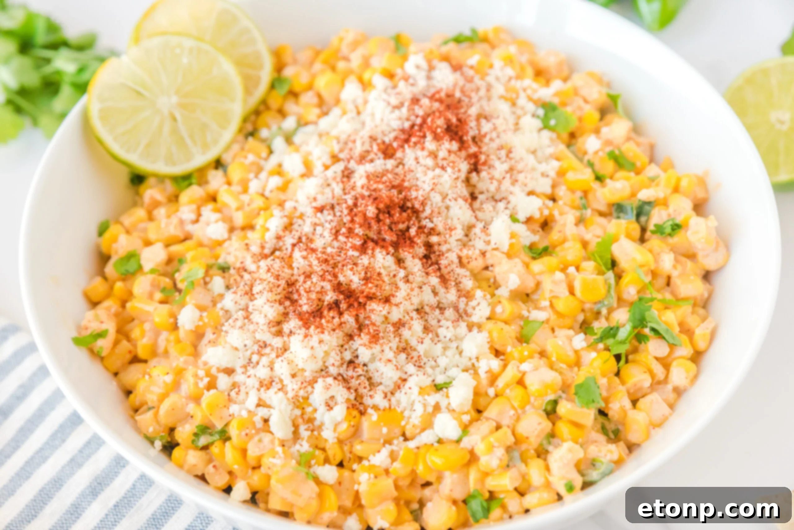 Mexican Street Corn Salad in a large white serving bowl, garnished with crumbled feta cheese and lime slices, ready for a gathering.