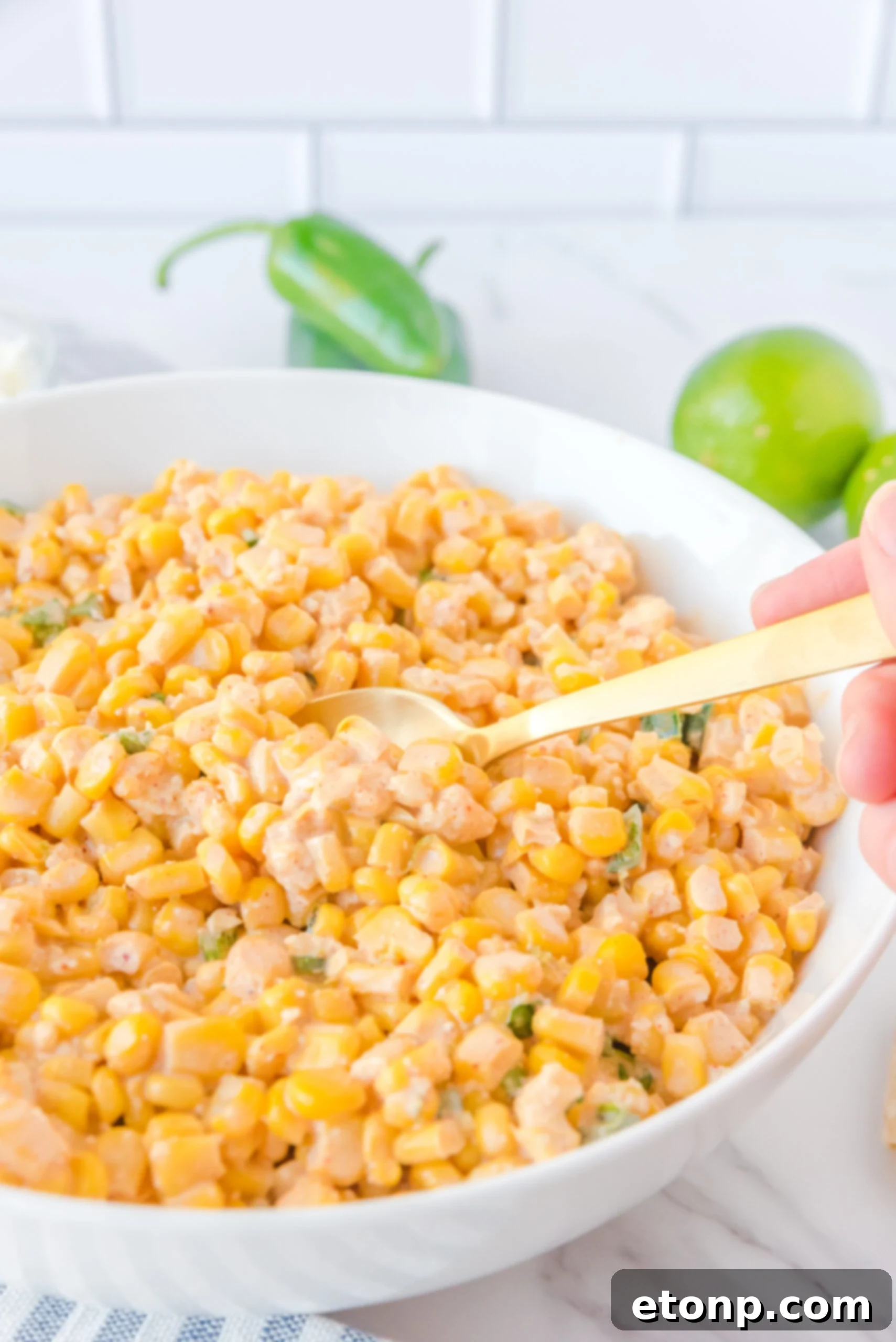 A gold spoon carefully removing a portion of Mexican Street Corn Salad from a large white serving bowl.
