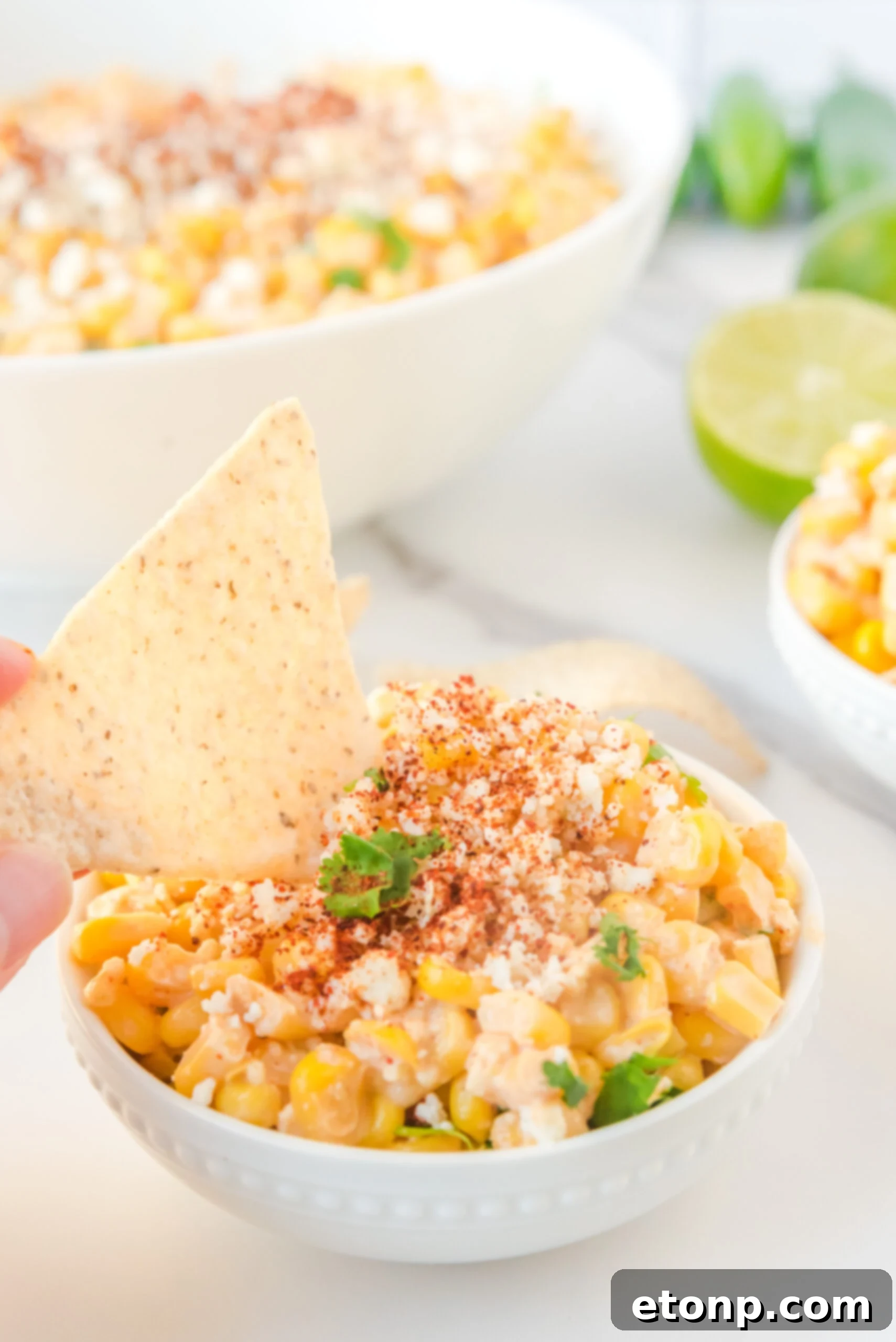 A crispy tortilla chip being dipped into a generous serving of Mexican Street Corn Salad, highlighting its creamy texture.