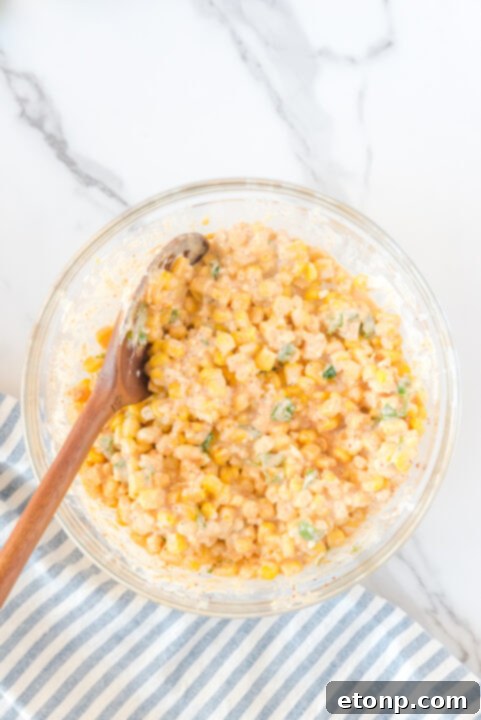Minced garlic being added to sautéed corn in a skillet, filling the air with aroma.