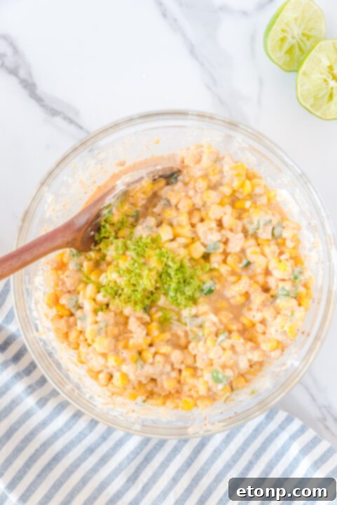 Diced jalapeno, mayonnaise, and heavy cream being mixed with cooked corn in a large bowl.