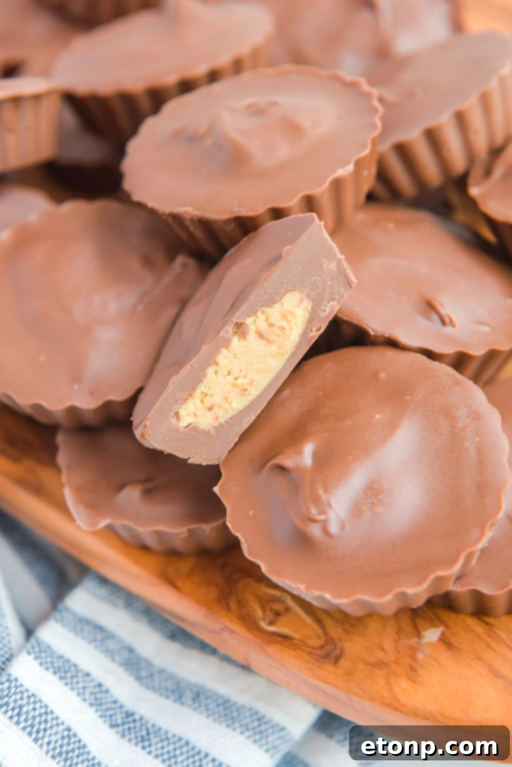 Homemade Peanut Butter Chocolate Cups 17 A stack of homemade Reese's Peanut Butter Cups on a rustic wooden serving board, with one cup featuring a bite revealing the creamy interior.