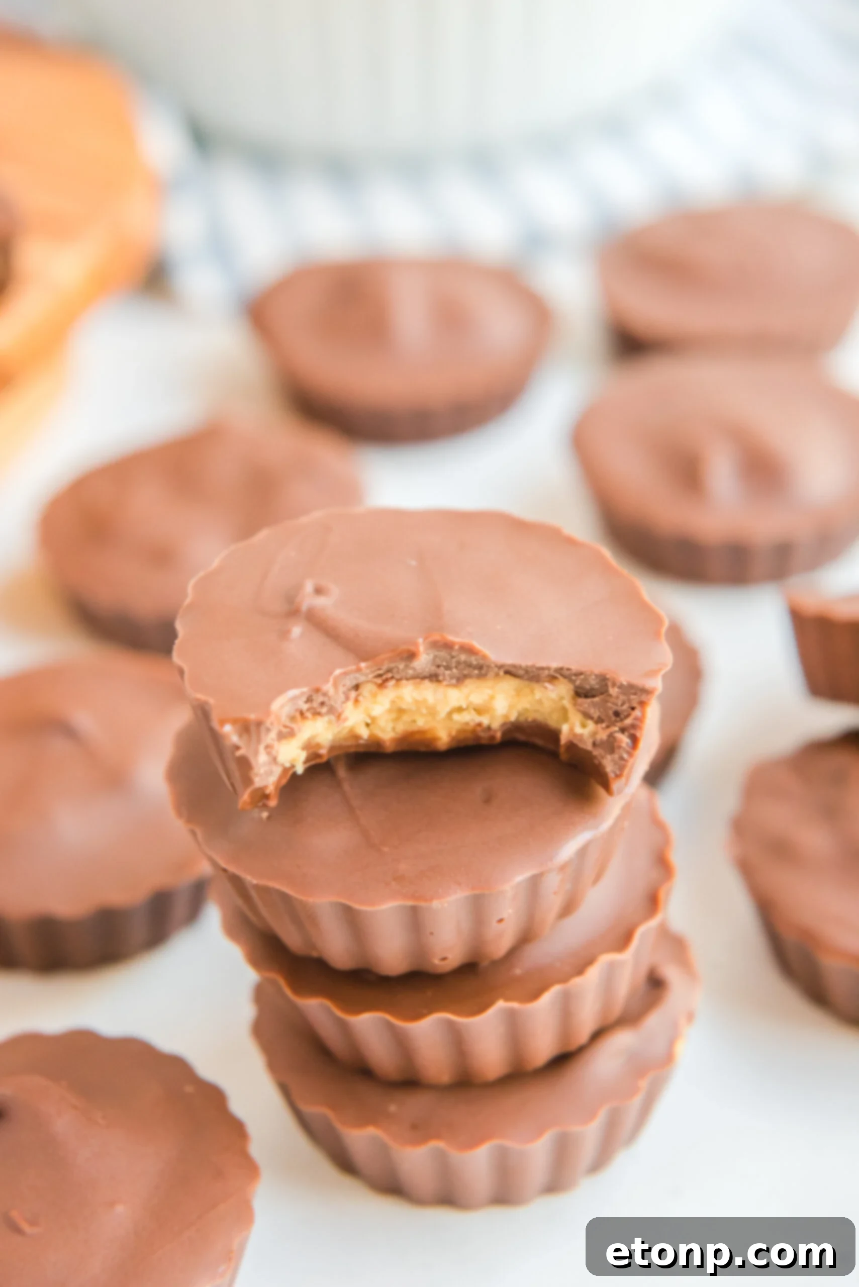 Homemade Peanut Butter Chocolate Cups 3 Four perfectly formed homemade Reese's Peanut Butter Cups stacked on a rustic wooden surface, with a bite taken from the top cup, showcasing the smooth peanut butter filling.
