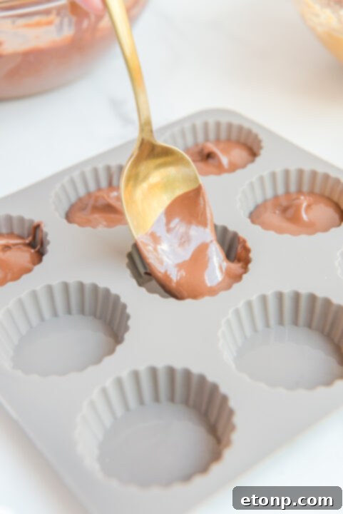 Homemade Peanut Butter Chocolate Cups 10 The final layer of melted chocolate being spooned over the peanut butter filling, smoothing out the top.