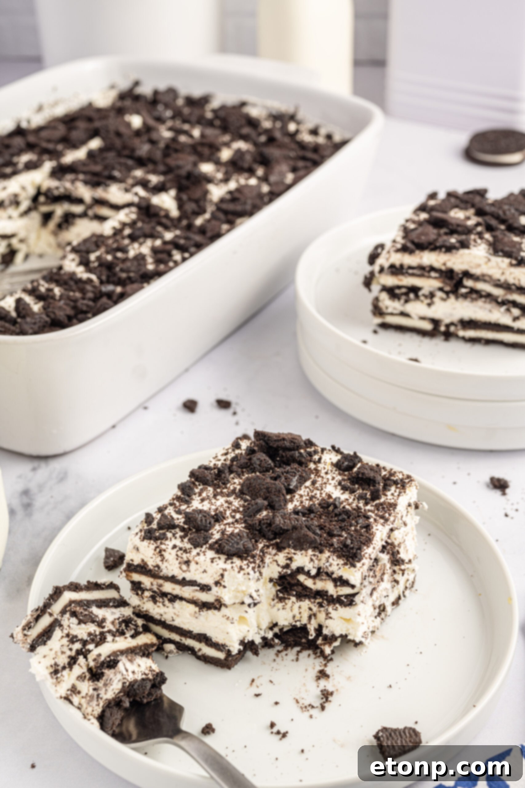 Oreo Cream Dream 22 Front view of a slice of Oreo Icebox Cake on a white plate with a bite removed by a silver fork.