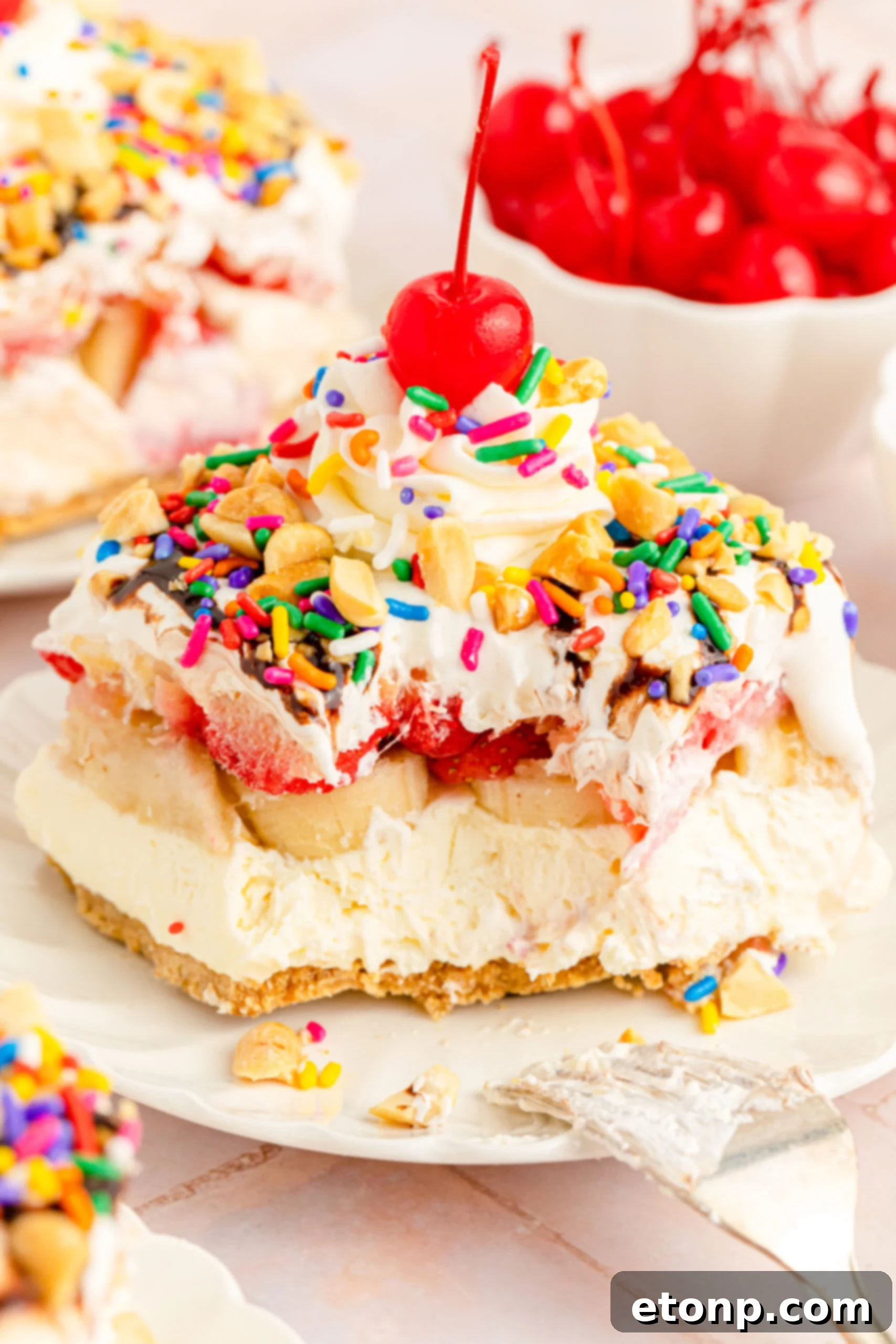 No-Bake Banana Split Bliss 15 Close up view of a slice of No Bake Banana Split Cake on a white plate with a bite removed by a silver fork, highlighting the toppings.