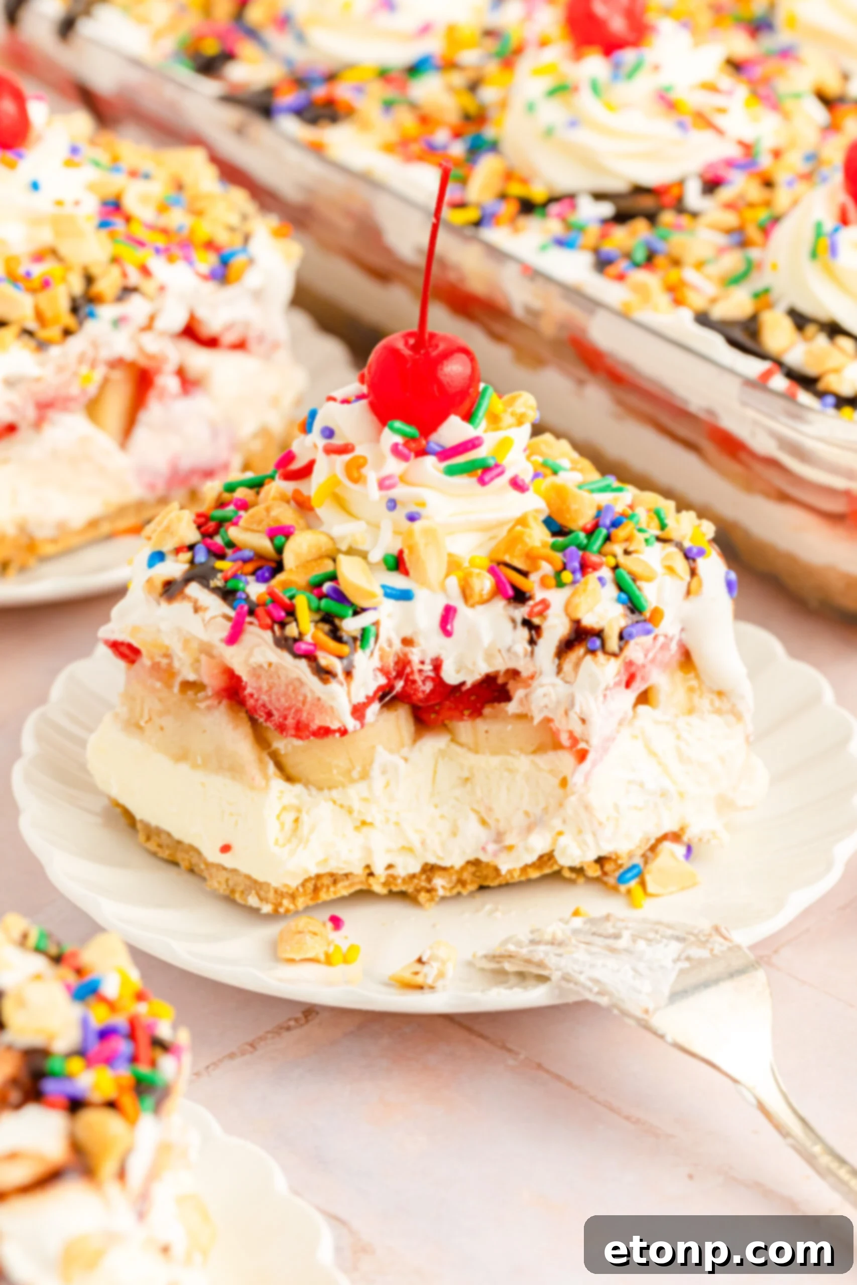 No-Bake Banana Split Bliss 17 Front view of a slice of No Bake Banana Split Cake on a white plate with a bite removed by a silver fork, showing the creamy filling.