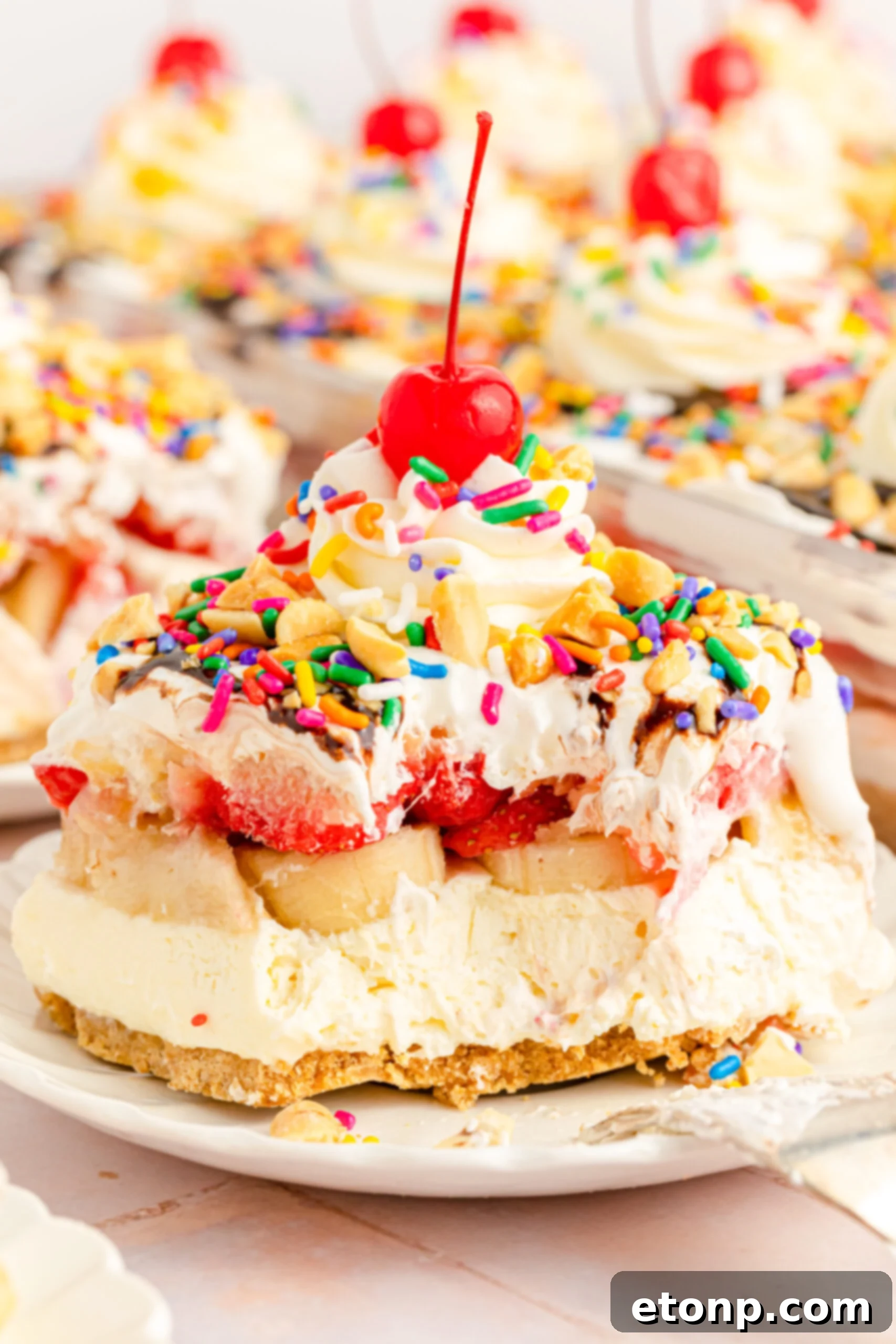 No-Bake Banana Split Bliss 18 Close up view of a slice of No Bake Banana Split Cake on a white plate with a bite removed by a silver fork, emphasizing the layers.