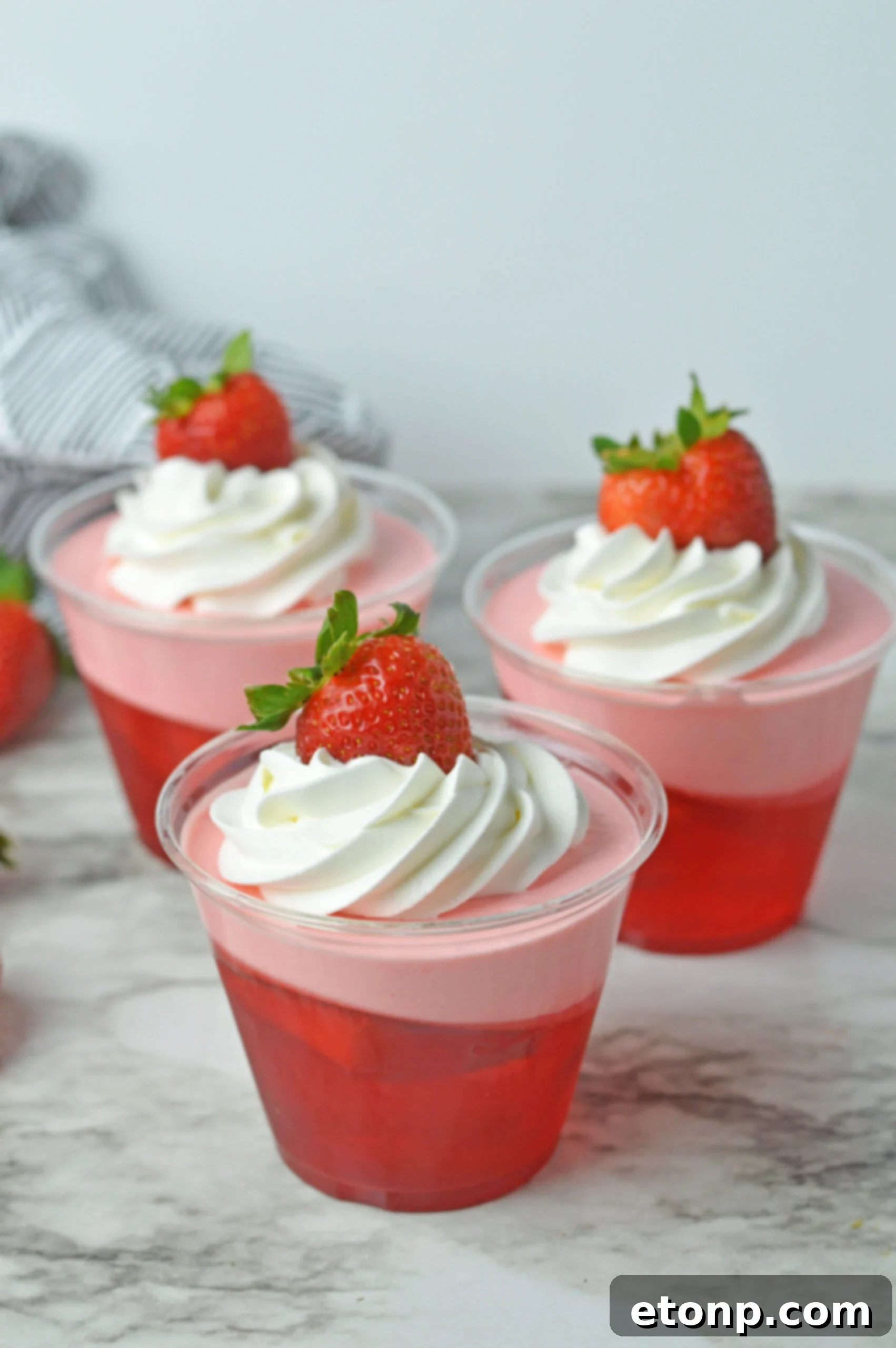 Strawberry Dream Parfaits 2 Front view of Strawberry Jello Parfait in plastic cups topped with whipped cream and a strawberry.