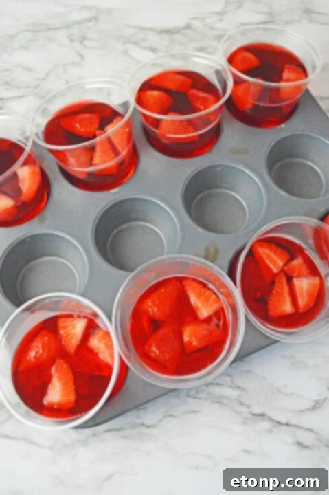 Strawberry Dream Parfaits 11 Pink jello and cool whip mixture being spooned into upright jello cups.