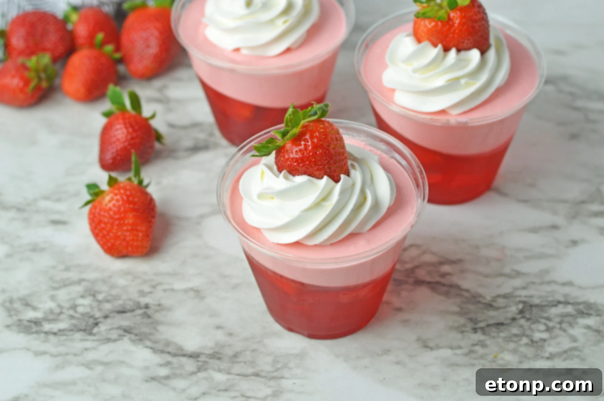 Strawberry Dream Parfaits 4 Front view of Strawberry Jello Parfait in plastic cups topped with whipped cream and a strawberry.