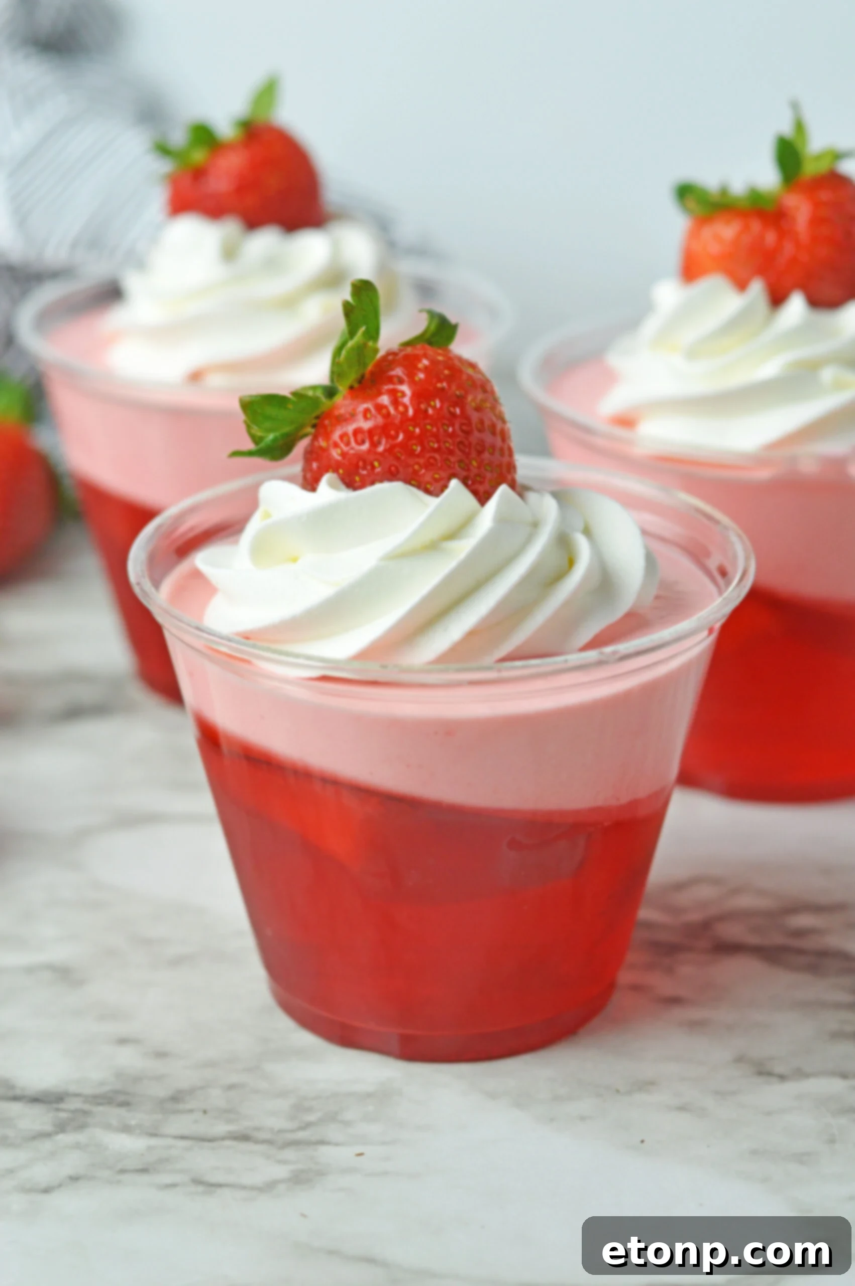 Strawberry Dream Parfaits 5 Front view of Strawberry Jello Parfait in plastic cups topped with whipped cream and a strawberry.