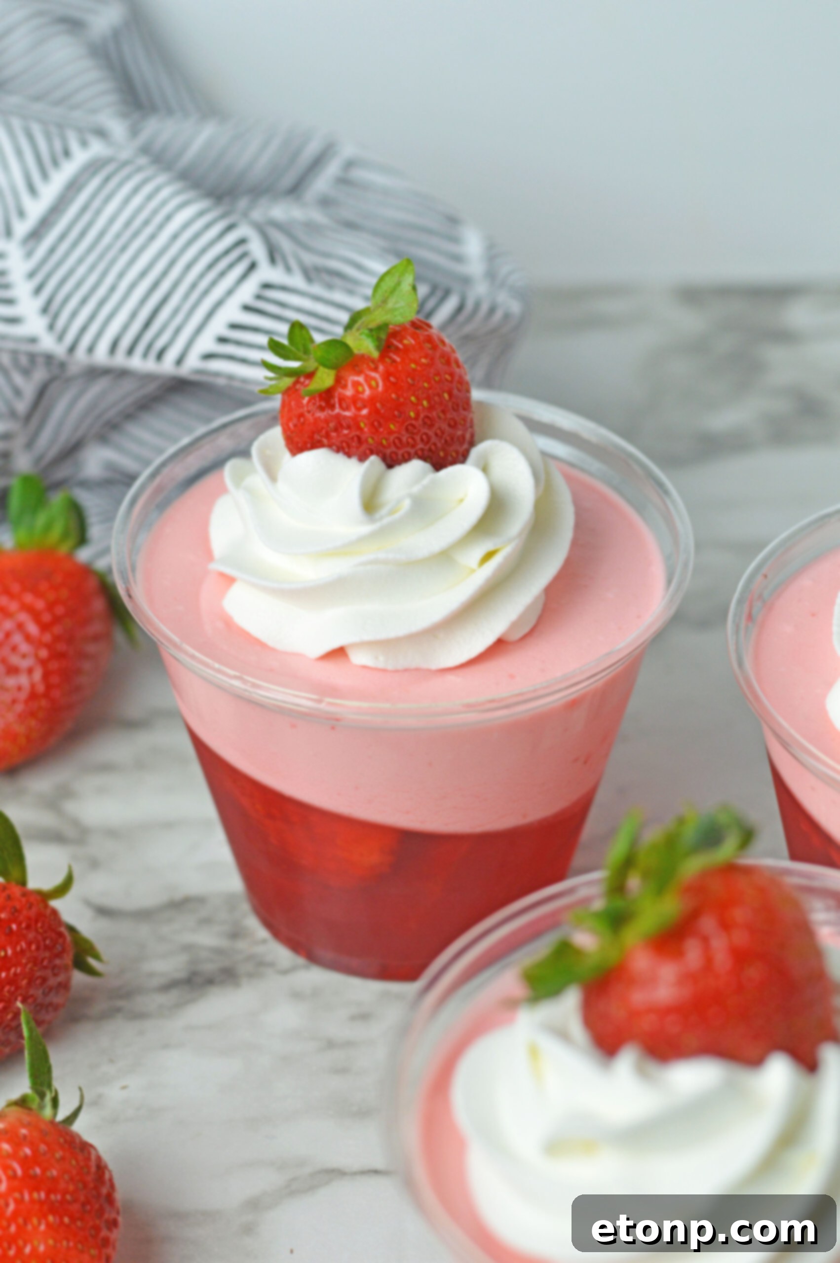 Strawberry Dream Parfaits 7 Close up view of Strawberry Jello Parfait in plastic cups topped with whipped cream and a strawberry.