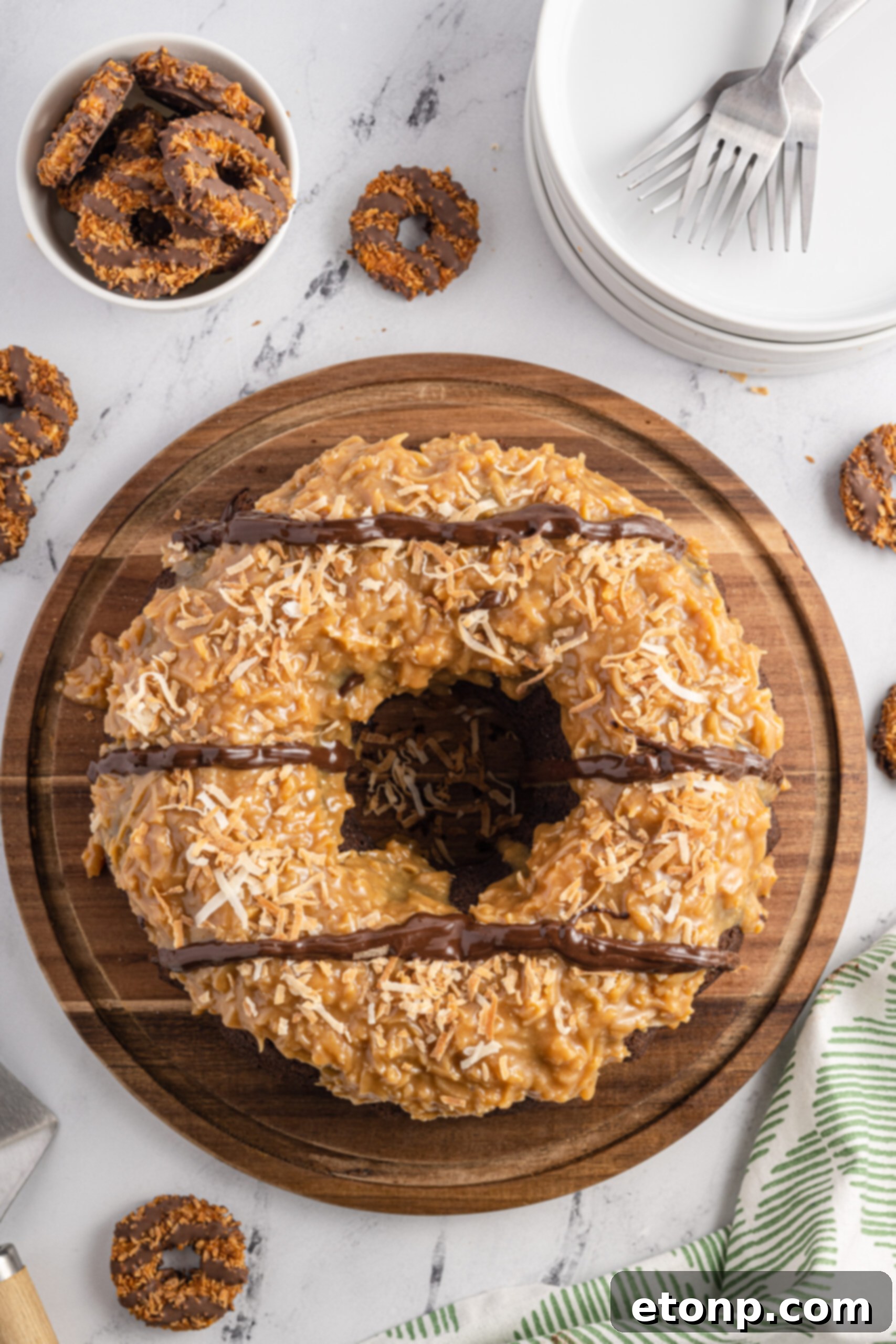 Overhead view of a beautifully decorated Samoa Cake on a rustic wooden cutting board, showcasing its signature caramel, toasted coconut, and chocolate drizzle topping.