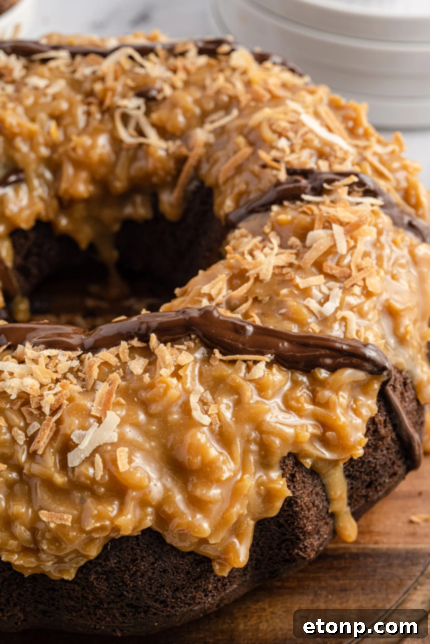 A close-up view of the Samoa Cake's decadent surface, highlighting the rich, glistening caramel, abundant toasted coconut flakes, and elegant chocolate drizzle.
