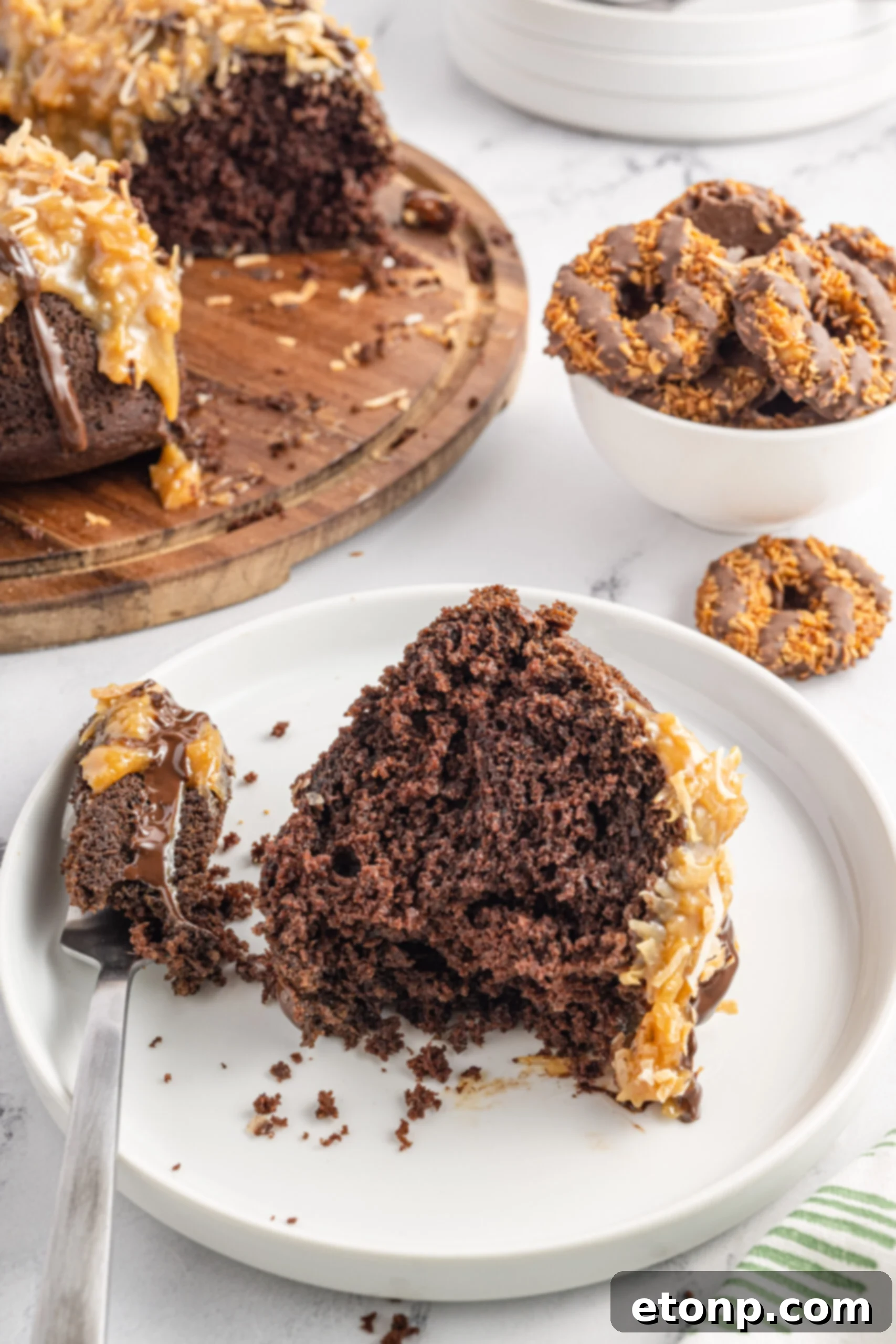 Front view of a slice of Samoa Cake on a white plate with a bite already taken by a silver fork, emphasizing its deliciousness, much like a perfectly portioned Samoa Cupcake.