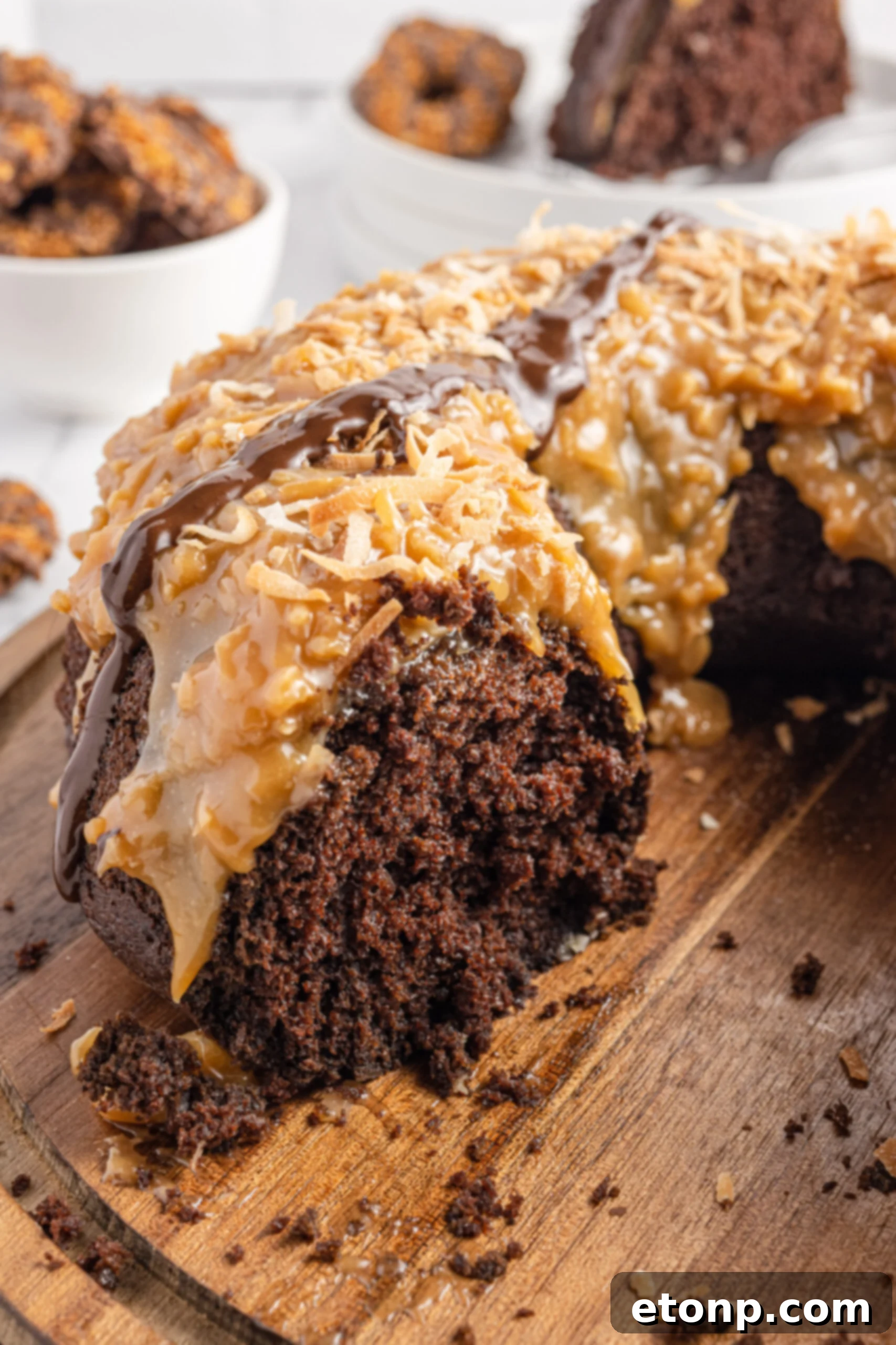 A Samoa Cake presented on a wooden board with a slice expertly removed, revealing the moist chocolate cake texture inside, beautifully contrasted with the vibrant caramel and coconut layers.