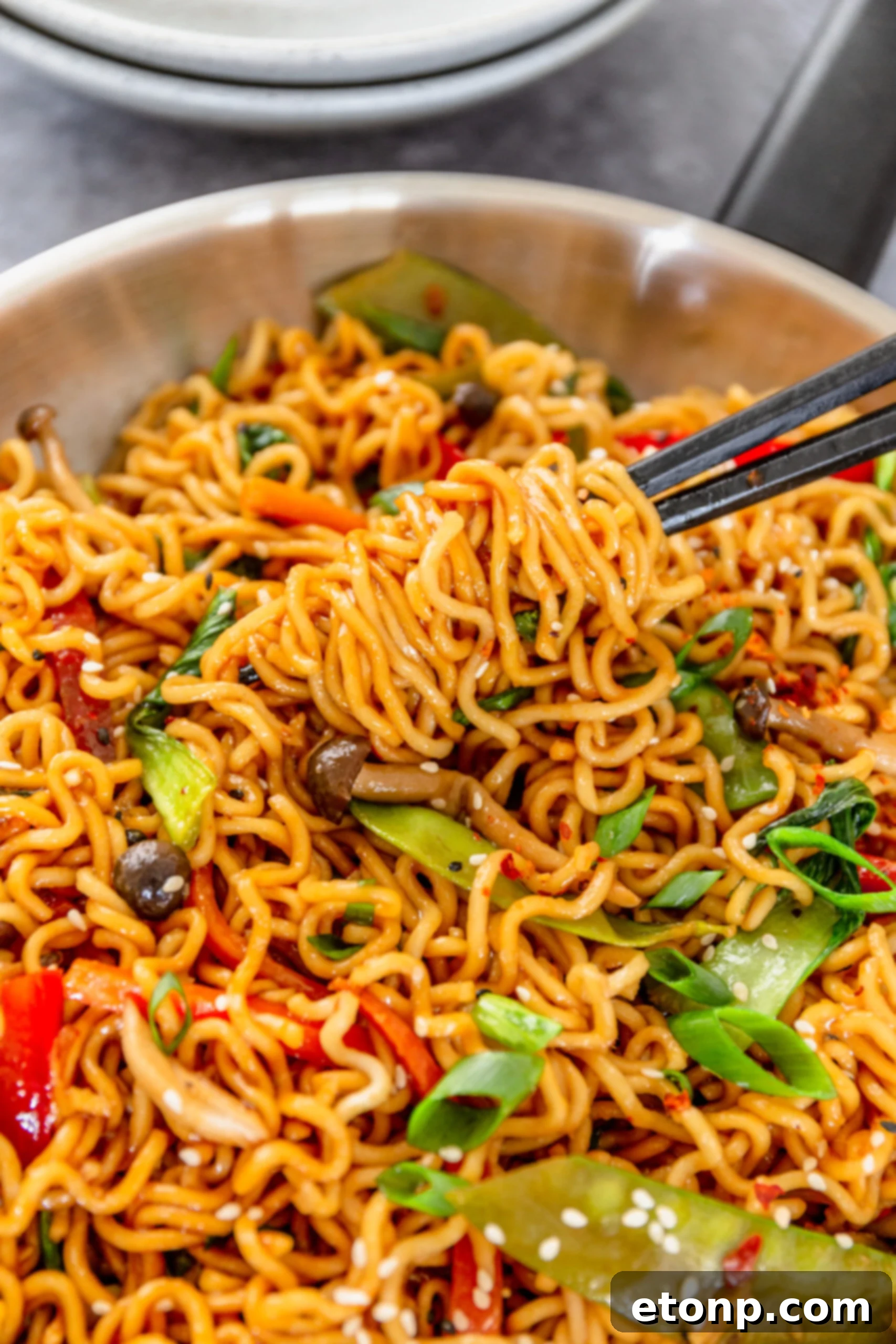 Chopsticks lifting a perfect bite of Ramen Stir Fry from a silver frying pan, illustrating the delicious combination of noodles and fresh vegetables.