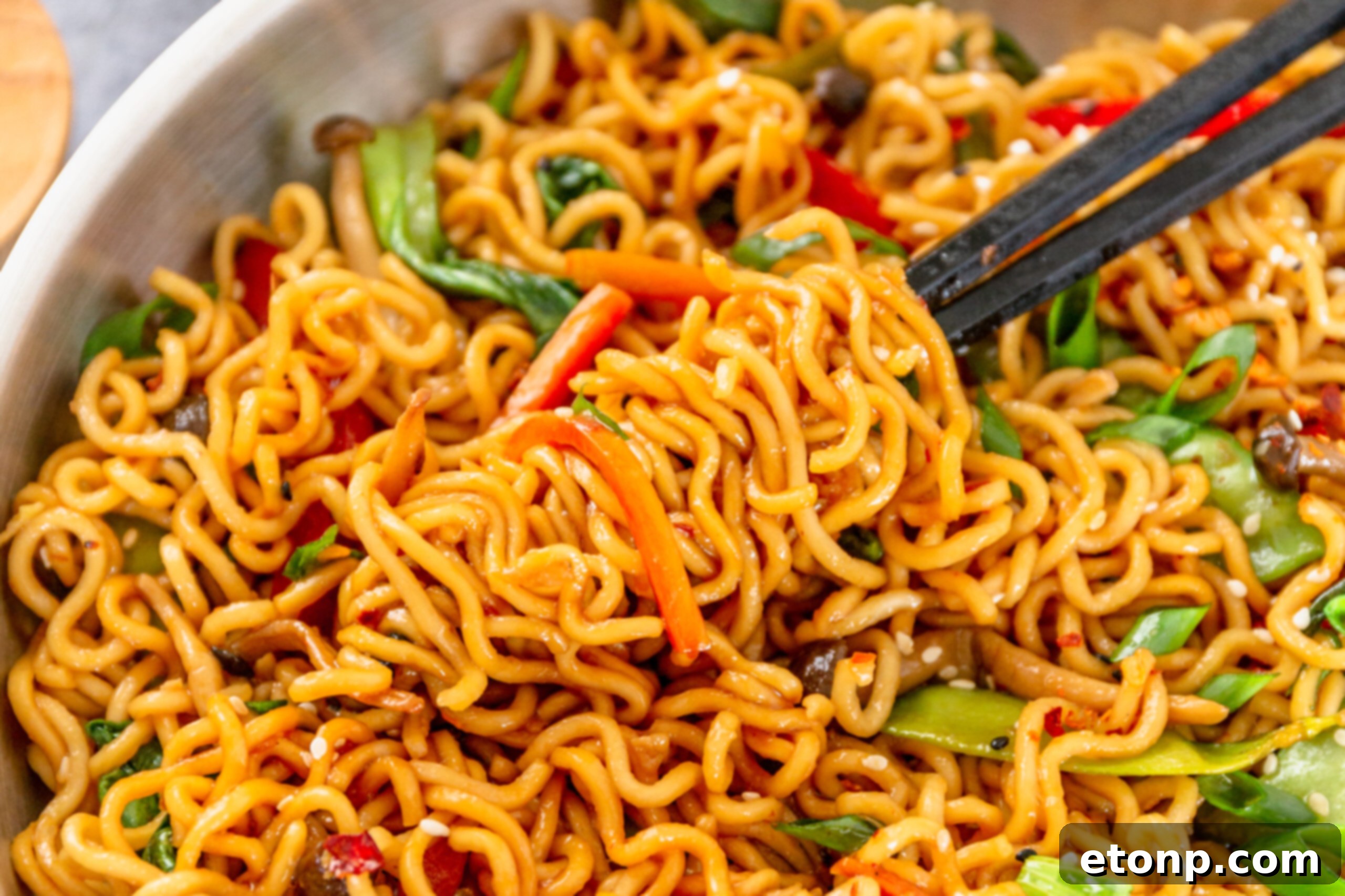 Chopsticks retrieving a portion of Ramen Stir Fry from a hot silver frying pan, showcasing the steam and freshness of the dish.