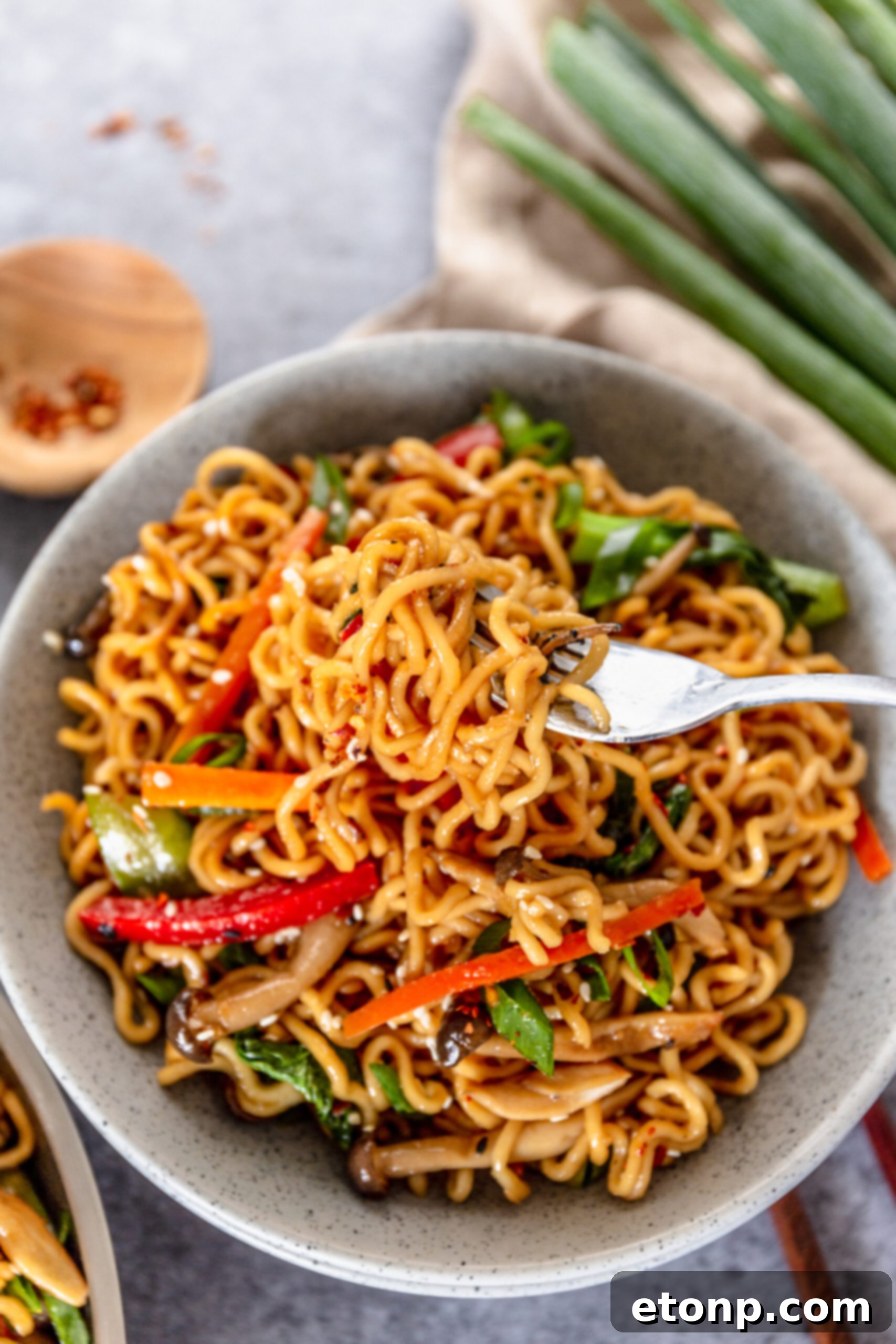 A fork lifting a delicious bite of Ramen Stir Fry from a speckled white bowl, ready to be enjoyed.