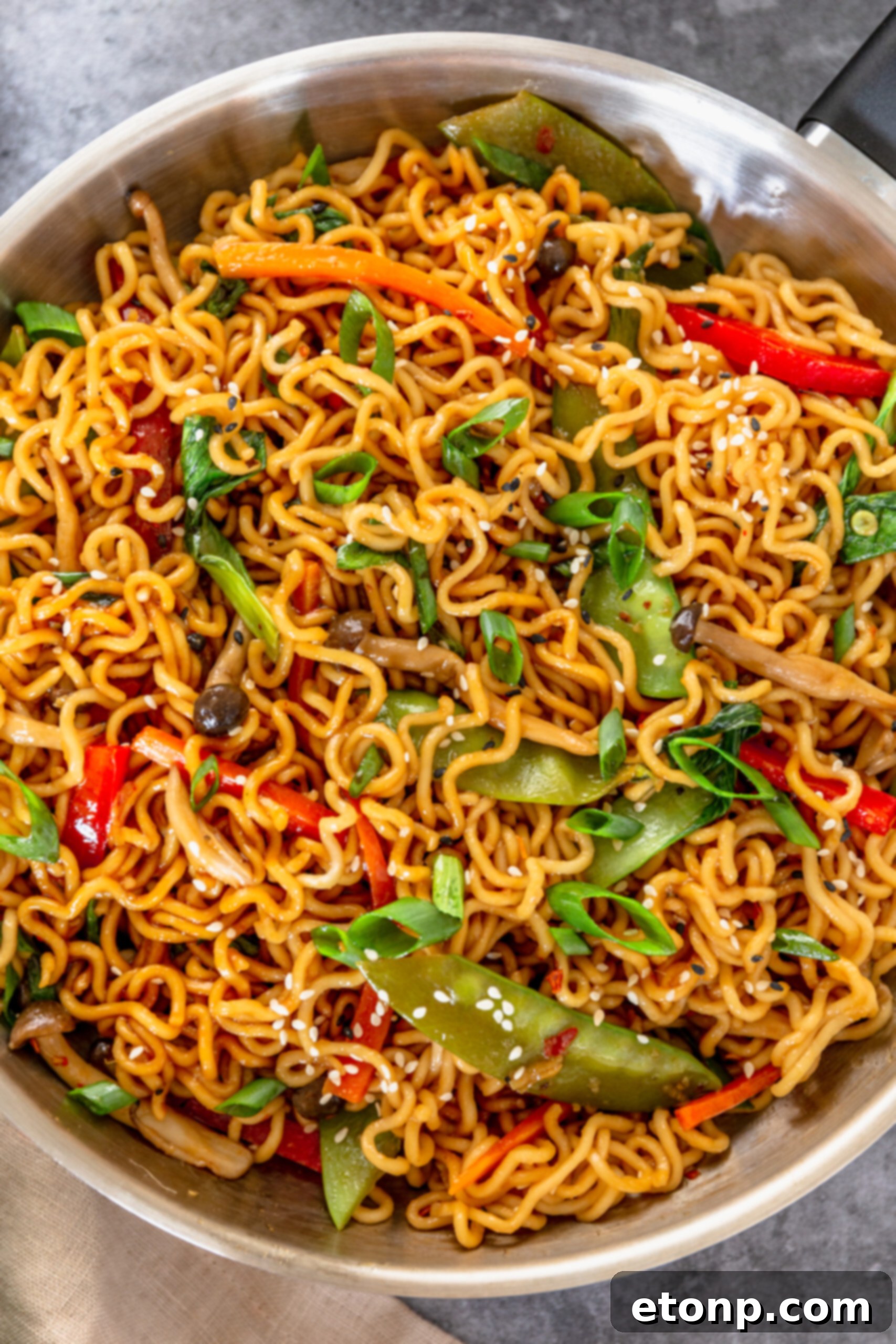 A silver frying pan showcasing the finished Ramen Stir Fry, beautifully garnished with sesame seeds, inviting a delicious meal.