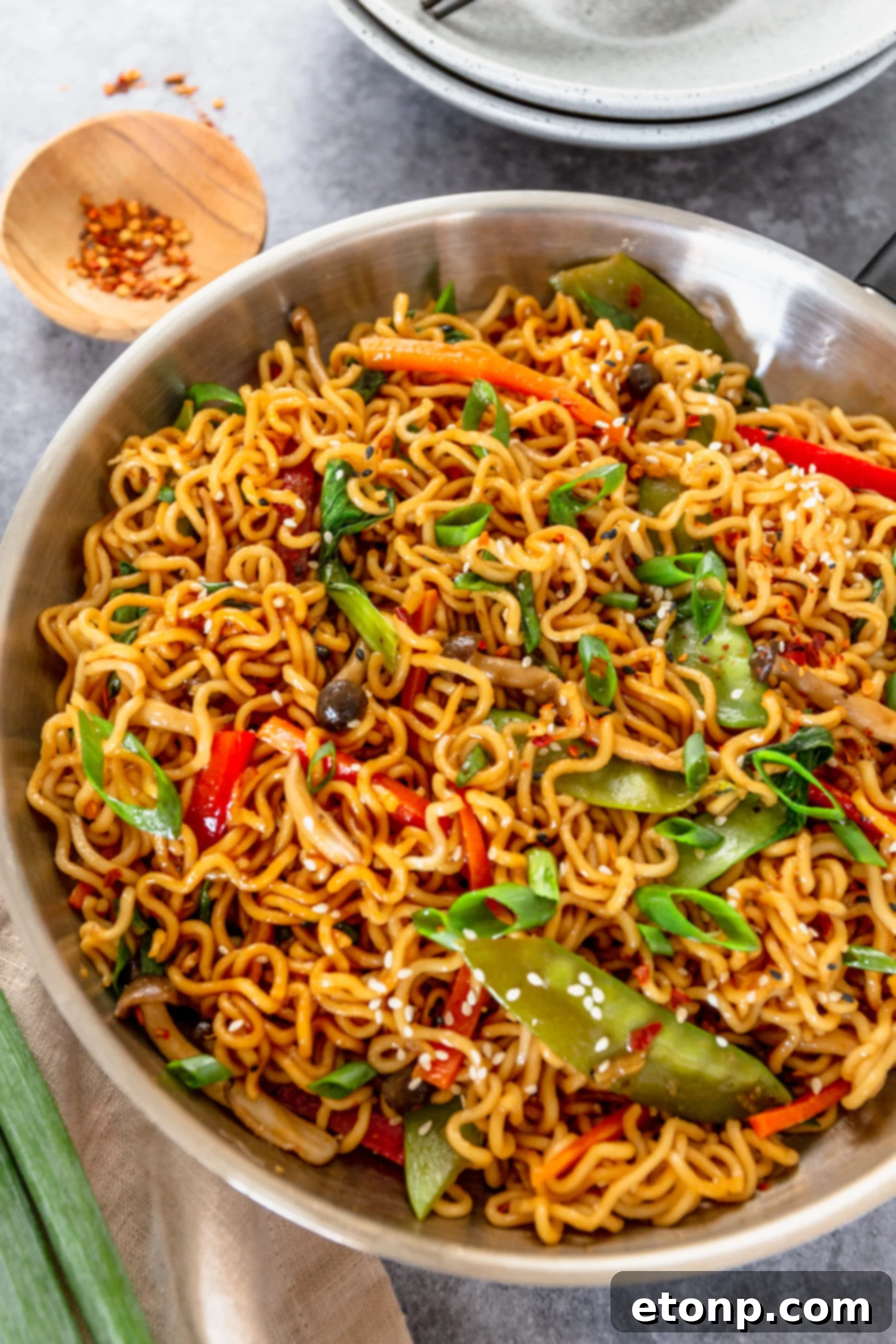 A silver frying pan filled with beautifully cooked Ramen Stir Fry, generously topped with toasted sesame seeds, ready to be served.