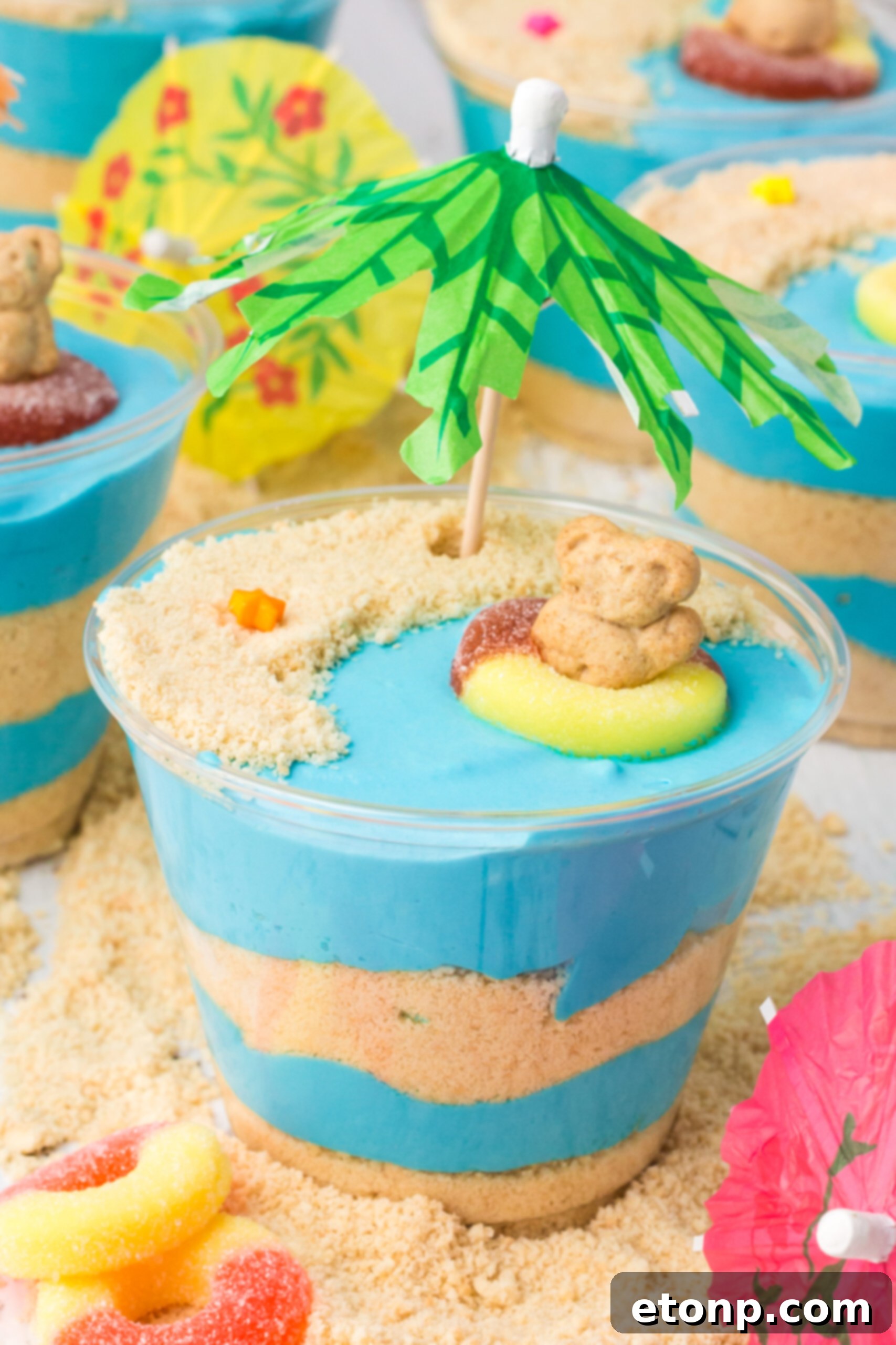 A top-down view of beautifully layered no-bake Beach Cheesecake Pudding Cups, showcasing the blue pudding and cookie 'sand'.