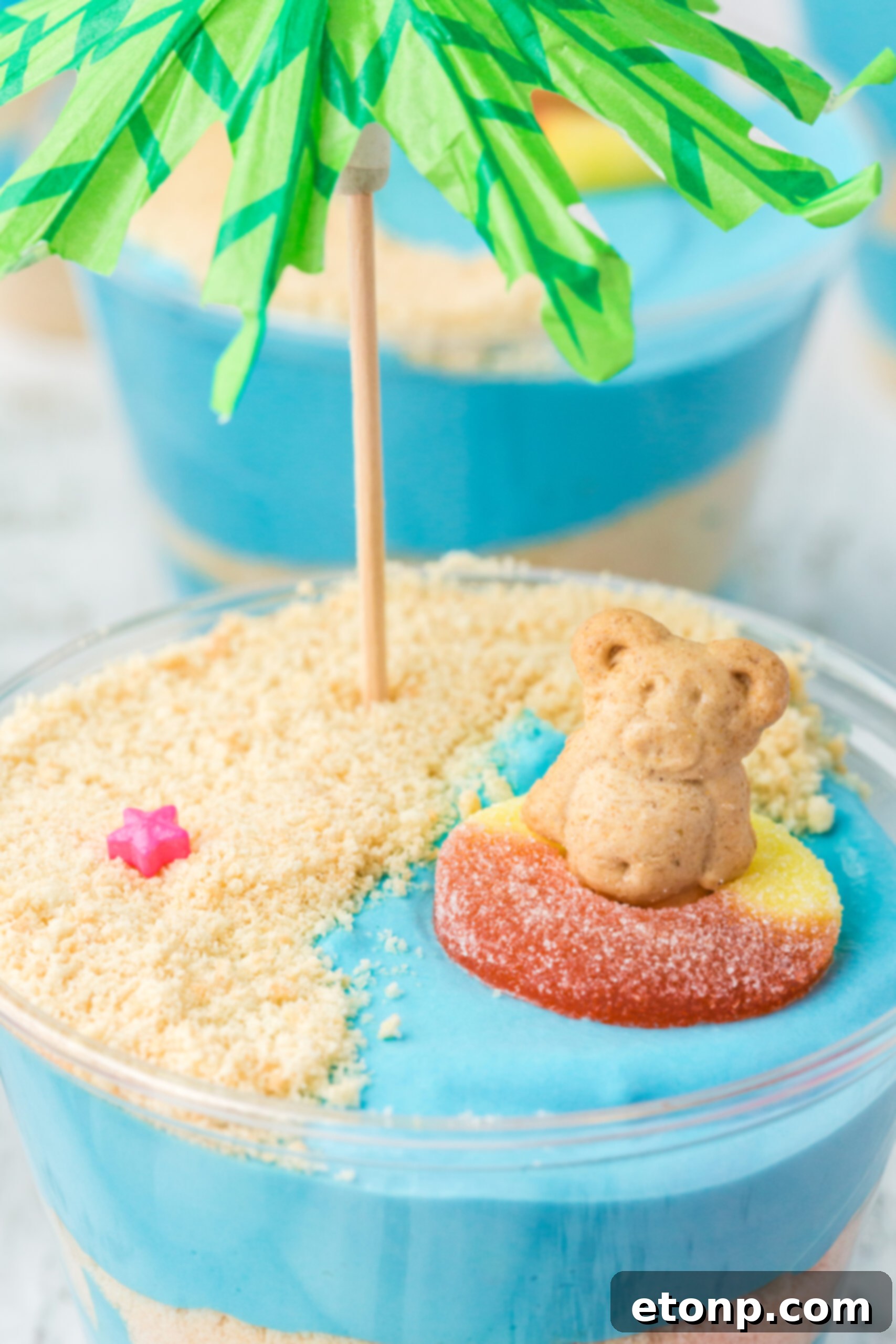 Close up view of Beach Cheesecake Pudding Cups with clear plastic spoons, showing the detail of the teddy grahams and gummy rings.