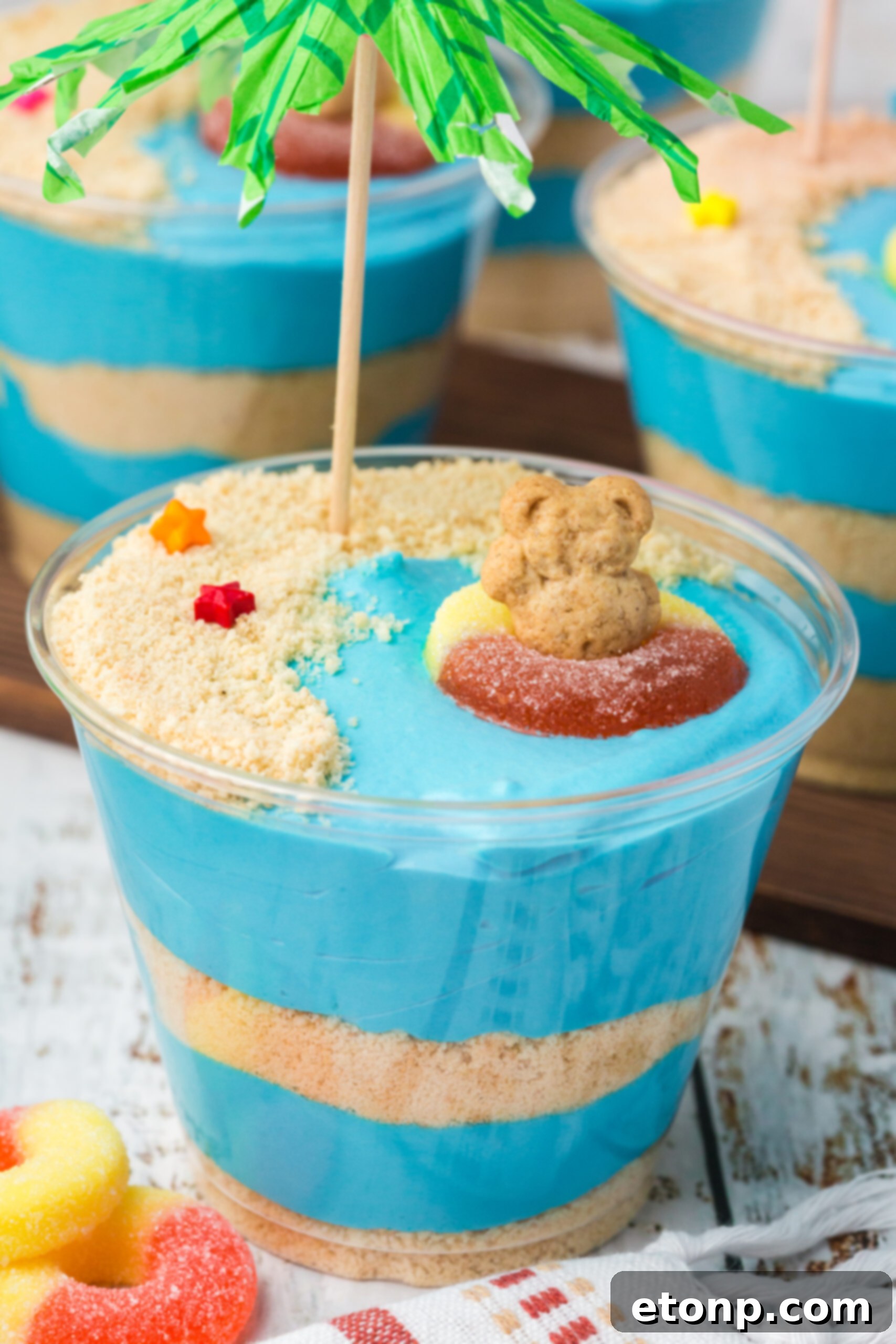 Close up view of Beach Cheesecake Pudding Cups on a white table, adorned with a small green umbrella, ready to be enjoyed.