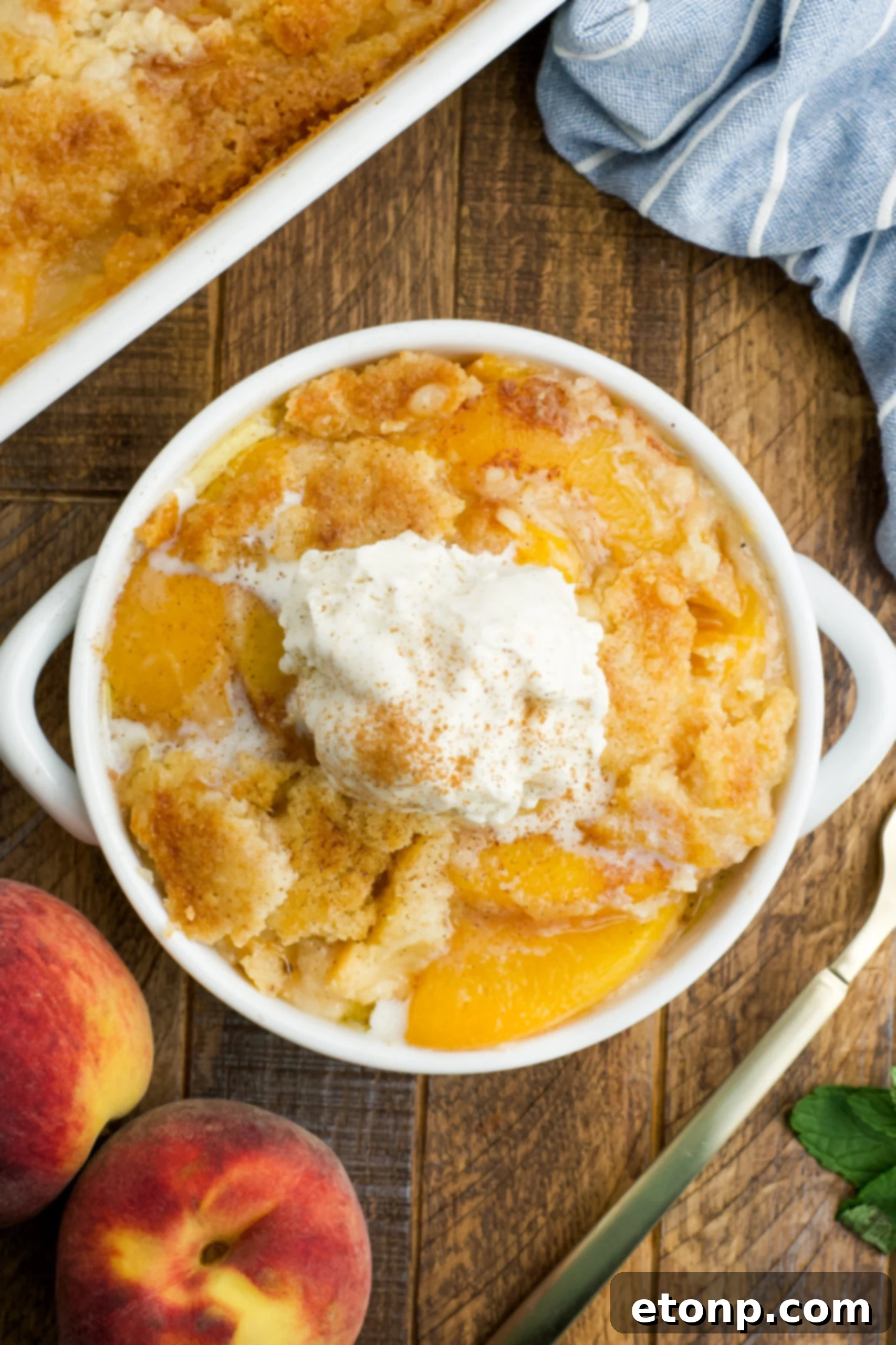 Overhead view of a serving of Peach Dump Cake in a white bowl topped with a scoop of vanilla ice cream.