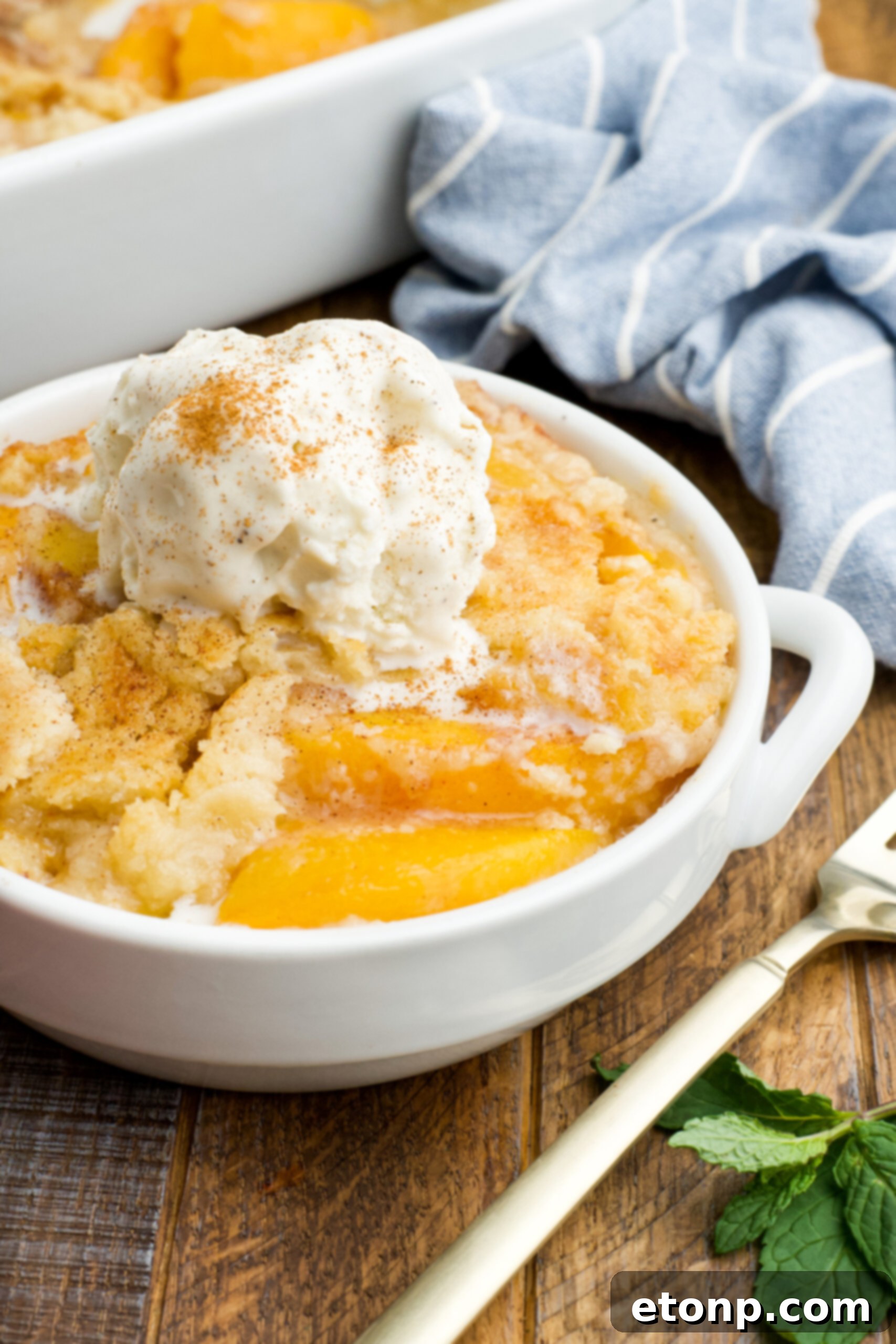 Front view of a serving of Peach Dump Cake in a white bowl topped with a scoop of vanilla ice cream.