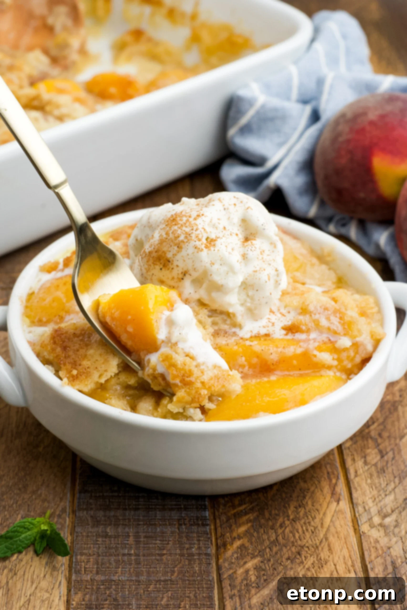 Front view of a serving of Peach Dump Cake in a white bowl with a gold fork removing a bite.