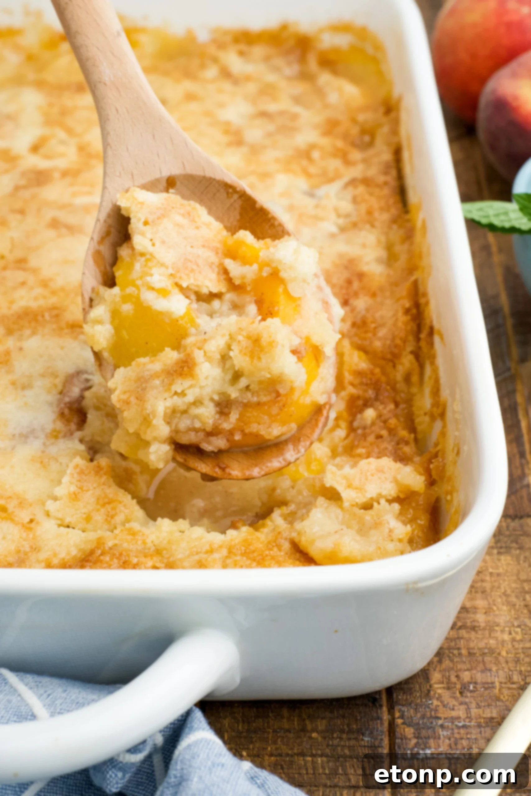 Close up view of a wooden spoon with a spoonful of Peach Dump Cake.